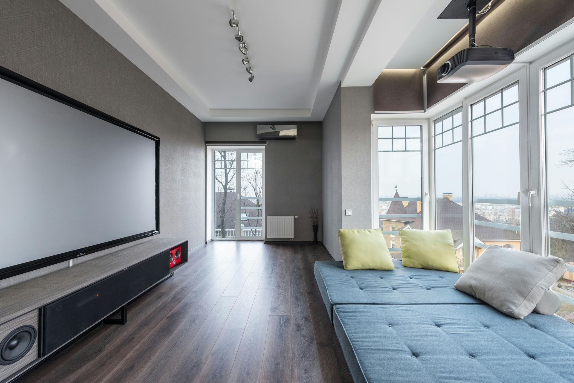 Modern living room with a projector screen, blue sofa, and large windows letting in daylight