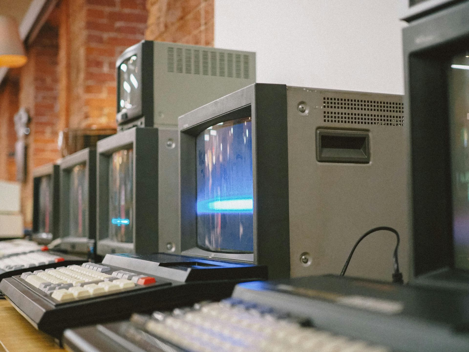 Row of old CRT monitors and keyboards on desks in a computer lab, with glowing screens.