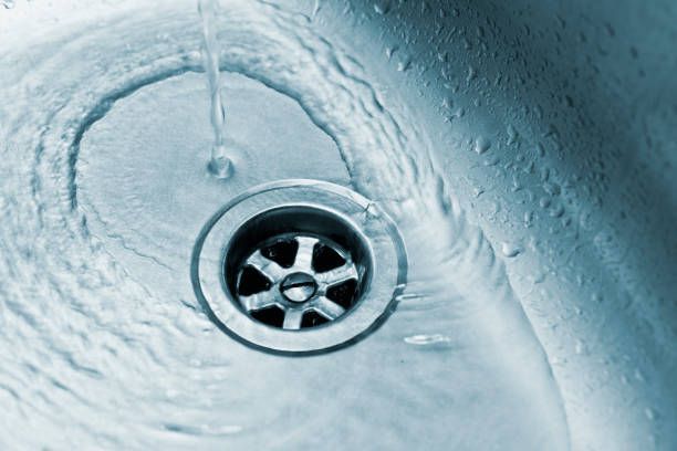 Water flows from a faucet into a stainless steel kitchen sink drain.