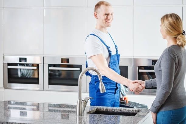 A technician in blue overalls shakes hands with a customer in a modern kitchen with stainless steel appliances. A technician in blue overalls shakes hands with a customer in a modern kitchen with stainless steel appliances.