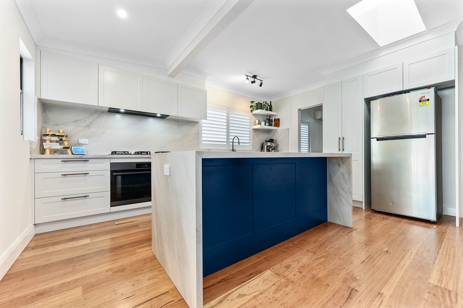 Modern kitchen with a blue island and wooden floors. White cabinets and a stainless steel fridge — Above & Beyond Interiors in Wollongong, NSW