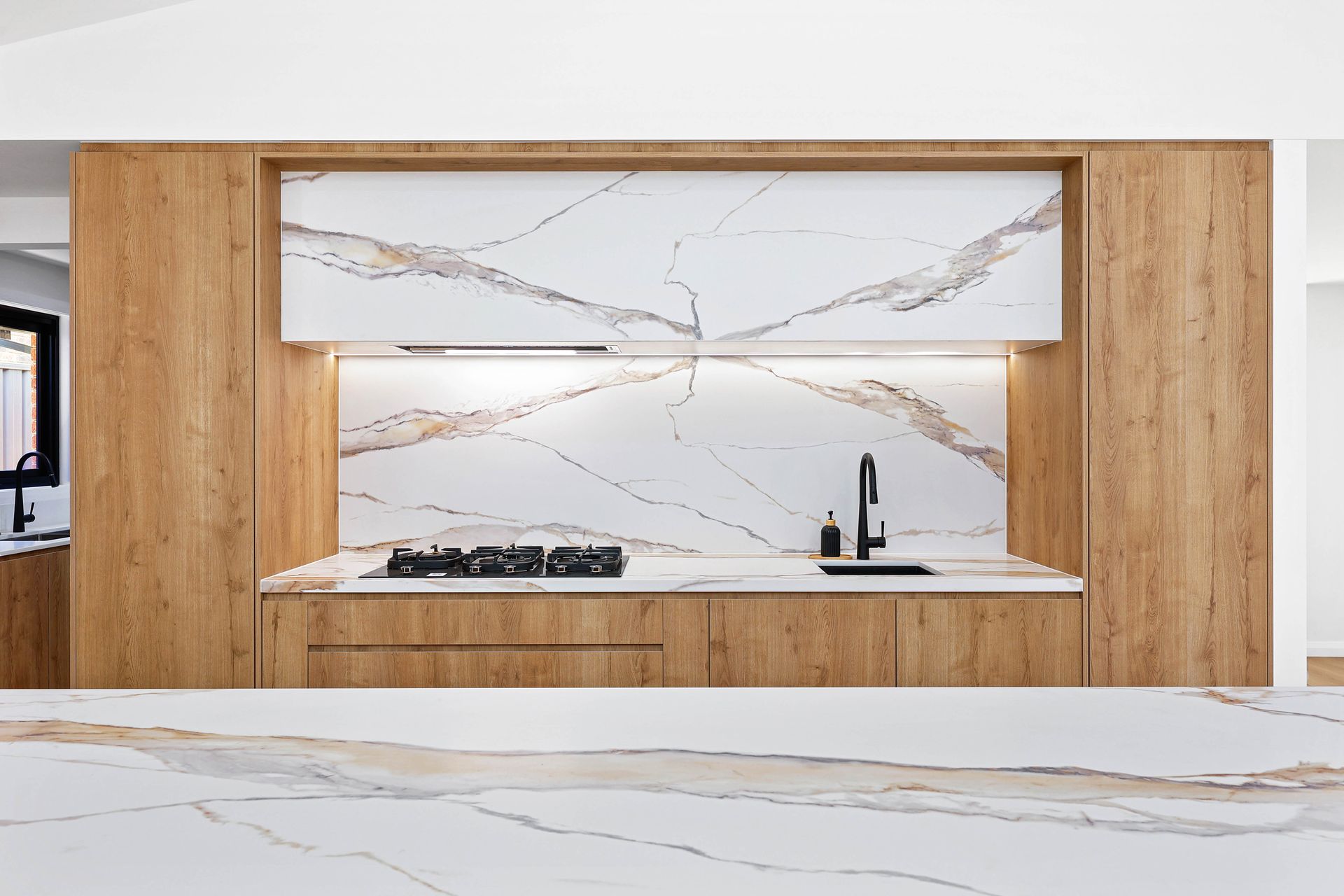 Modern kitchen with wood cabinets, marble backsplash, and black faucet — Above & Beyond Interiors in Southern Highlands, NSW