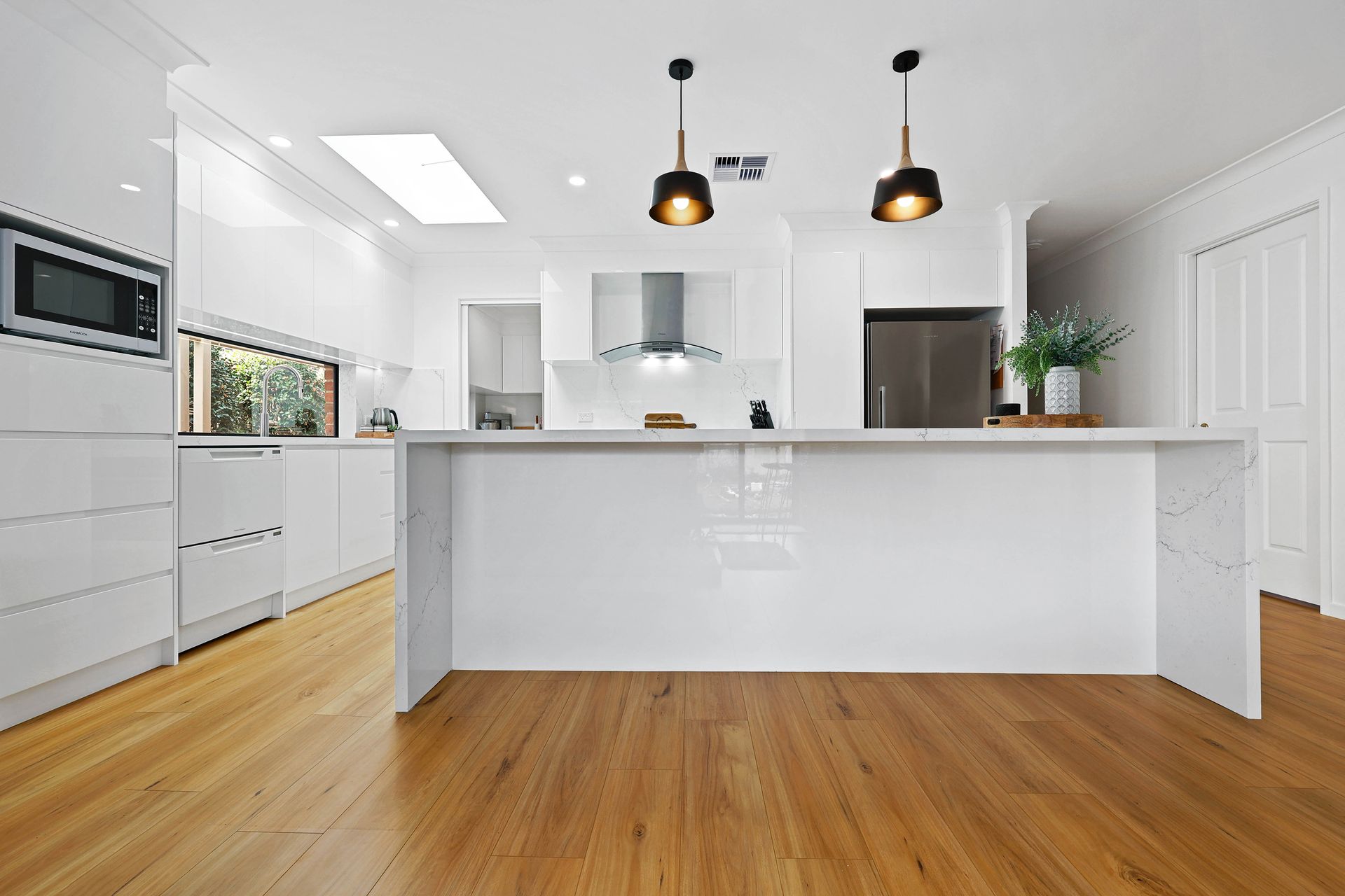 Modern white kitchen with wooden floors, island, and stainless steel refrigerator — Above & Beyond Interiors in Narellan, NSW