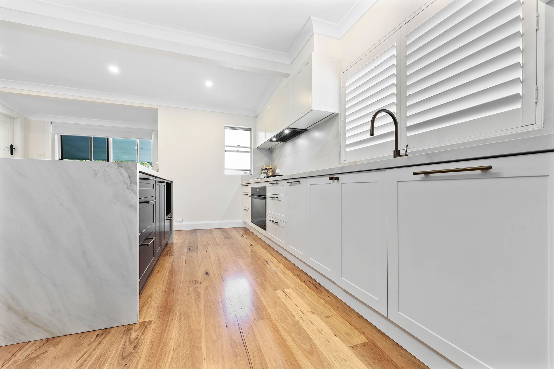 Bright white modern kitchen with wood floors, marble island, and shuttered windows — Above & Beyond Interiors in Wollongong, NSW