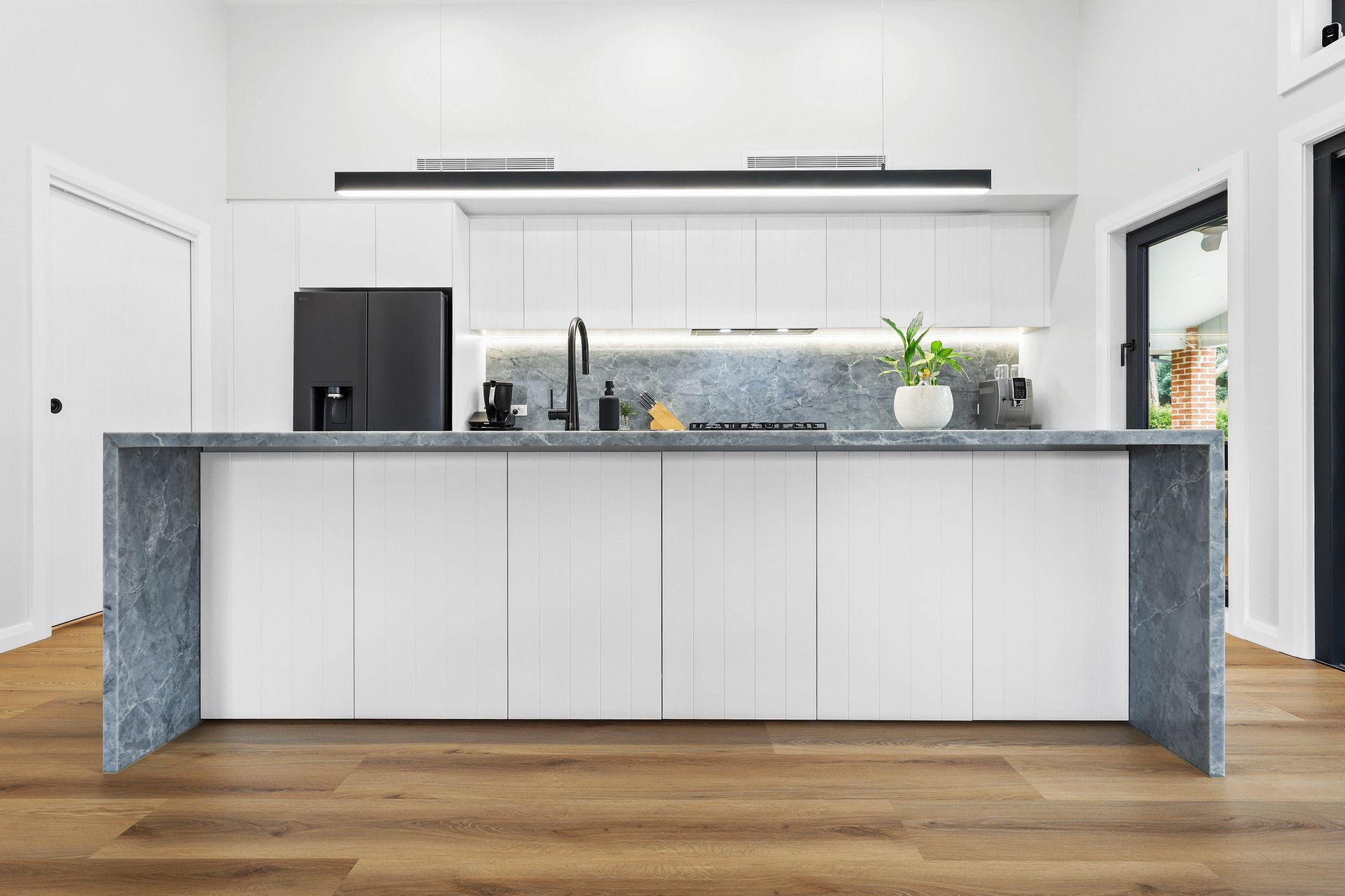 Modern white kitchen with wood floors, grey countertop, and a stainless steel oven — Above & Beyond Interiors in Wollongong, NSW