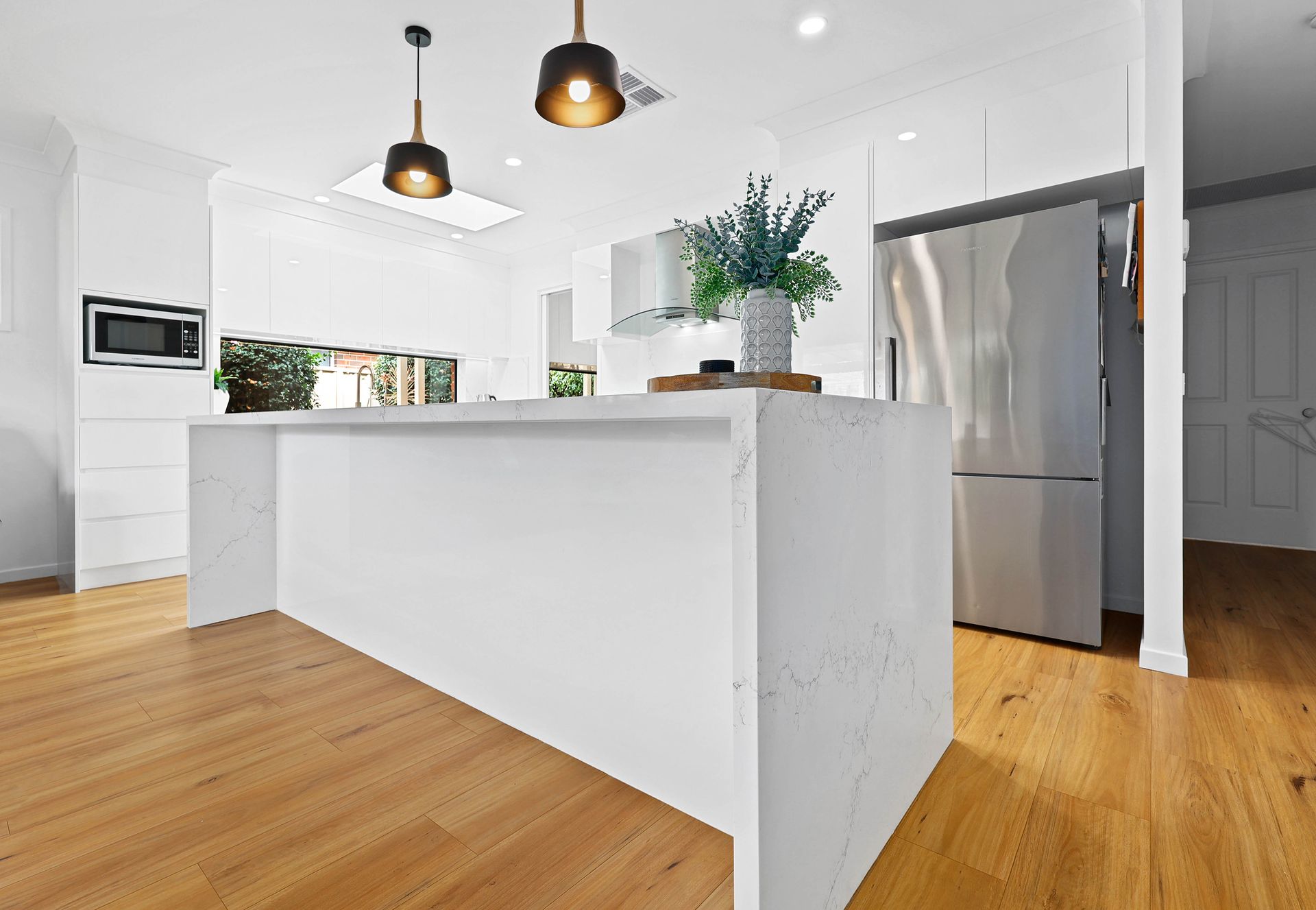 Modern white kitchen with island and hardwood floors — Above & Beyond Interiors in Smeaton Grange, NSW
