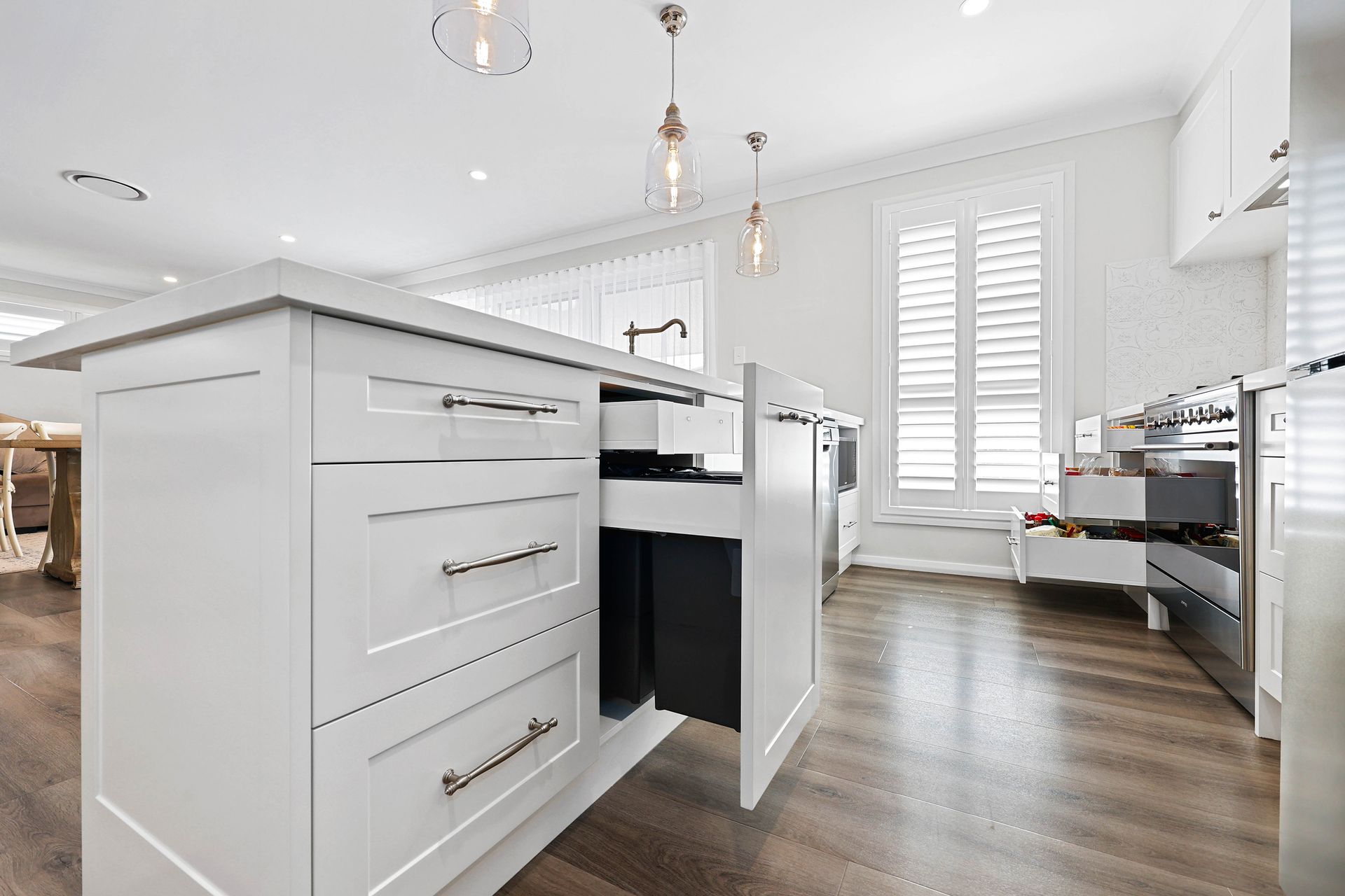White kitchen island with open trash drawer, drawers, and hardwood floor — Above & Beyond Interiors in Smeaton Grange, NSW