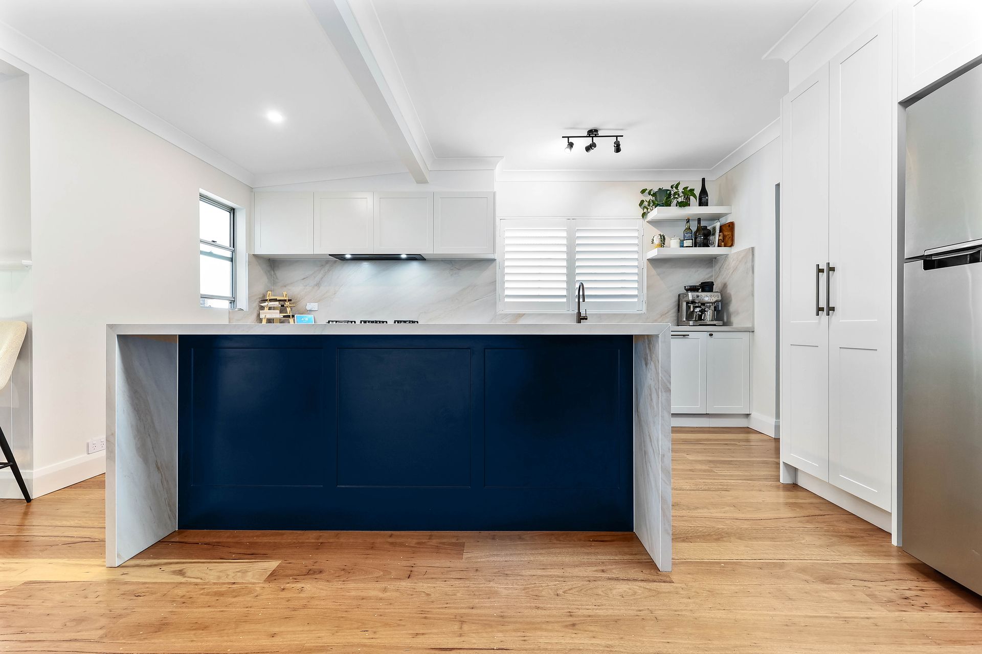 Modern kitchen with blue island, white cabinets, wood floor, and stainless steel refrigerator — Above & Beyond Interiors in Wollongong, NSW