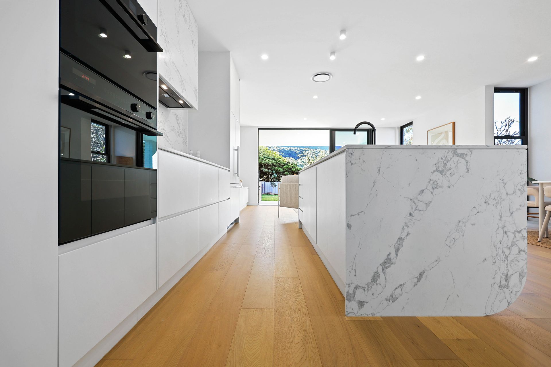 Modern white kitchen with a marble island and wooden floors — Above & Beyond Interiors in Southern Highlands, NSW