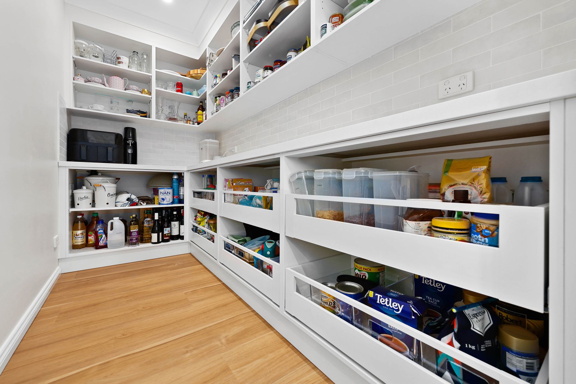 White pantry with pull-out drawers, shelves, and various food items. Wooden floor and white walls — Above & Beyond Interiors in Mount Annan, NSW