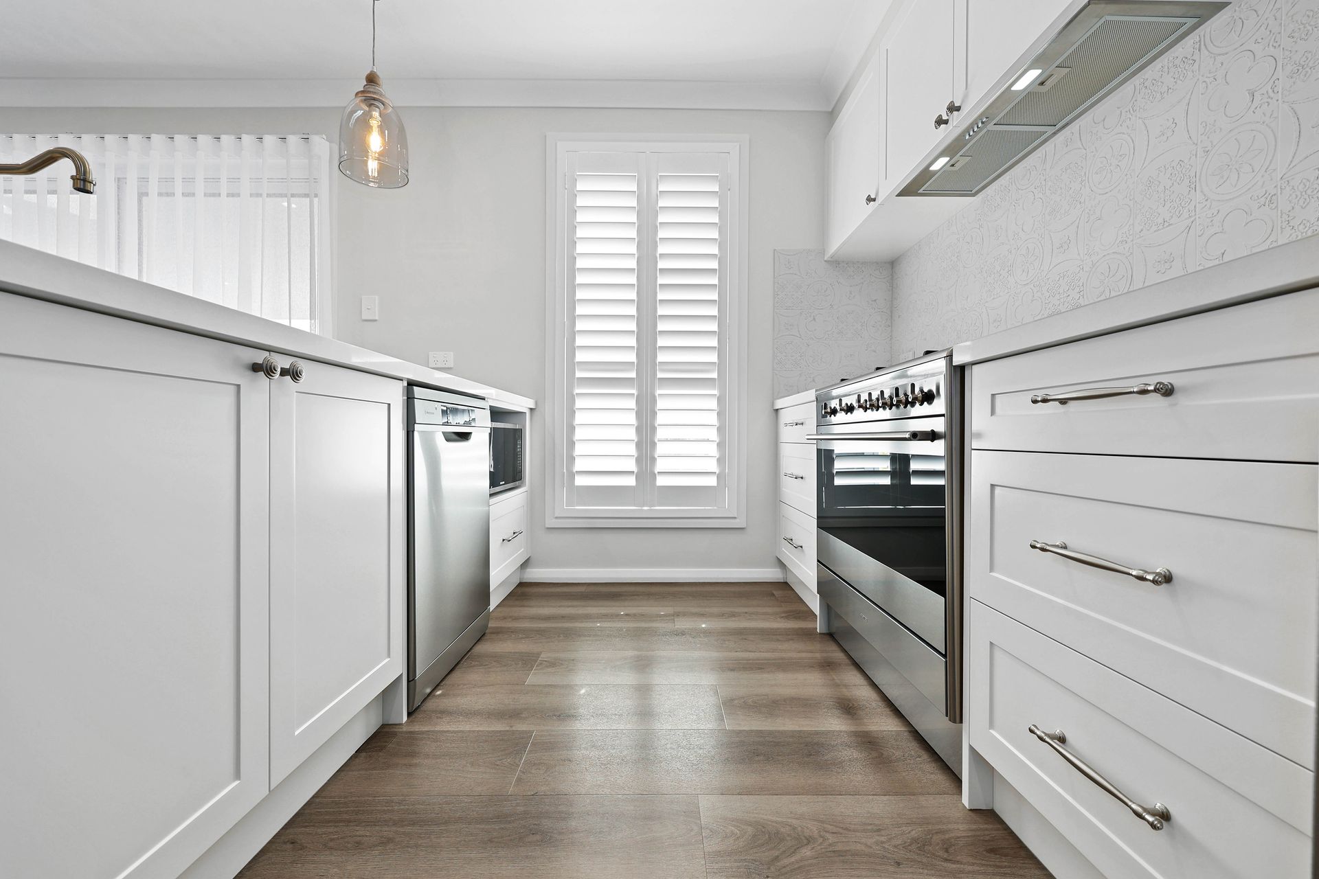 White kitchen with stainless steel appliances and shuttered window — Above & Beyond Interiors in Picton, NSW