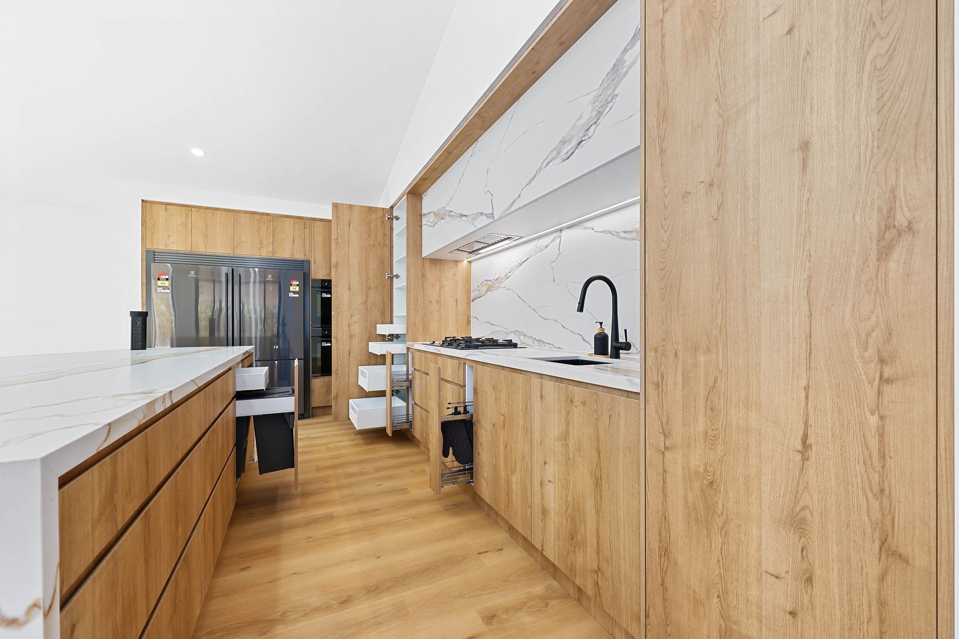 Modern kitchen with light wood cabinets, marble countertops, and a stainless steel refrigerator — Above & Beyond Interiors in Narellan, NSW