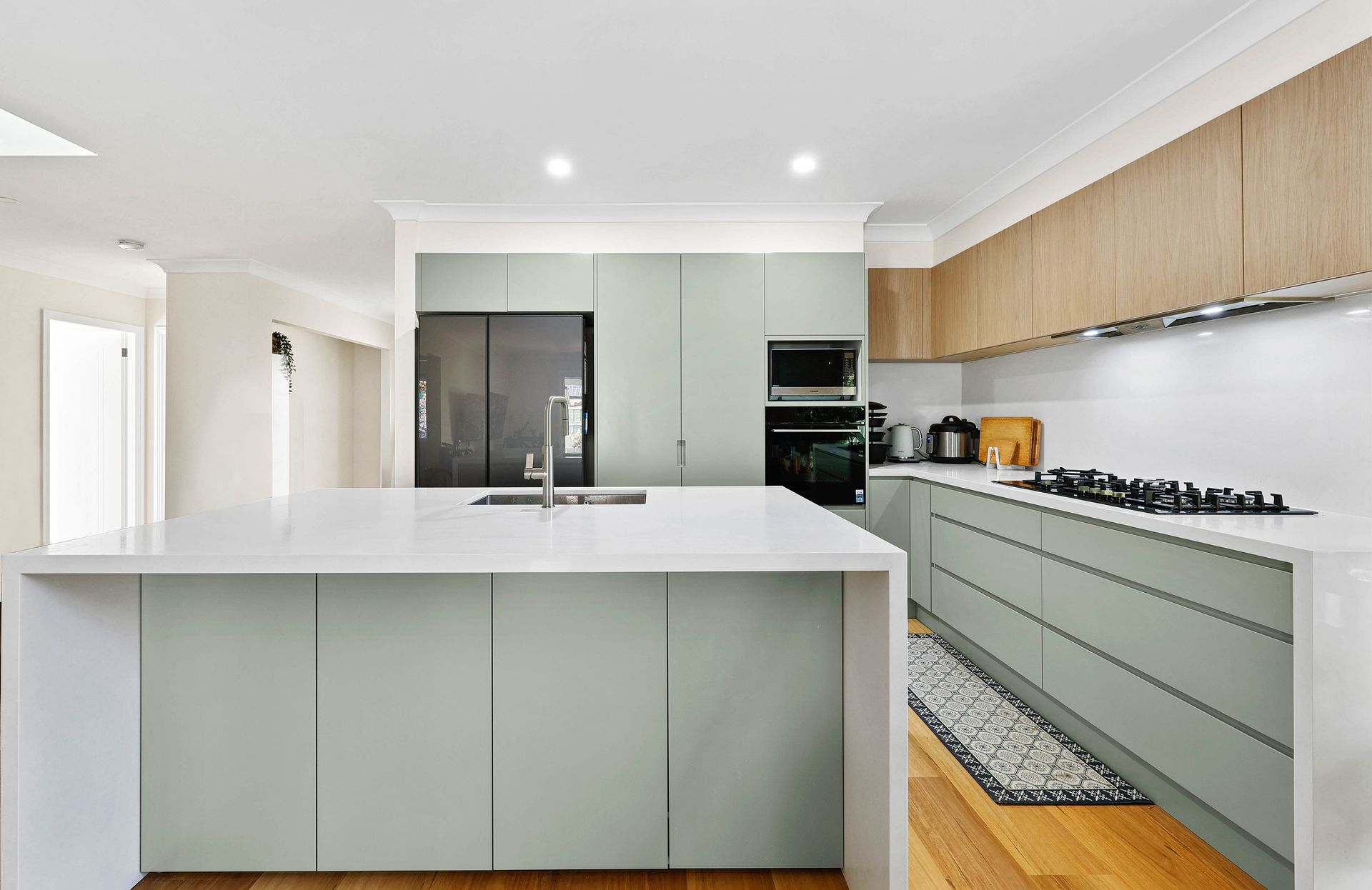 Modern kitchen with light green cabinets, white countertops, and wooden floors — Above & Beyond Interiors in Southern Highlands, NSW