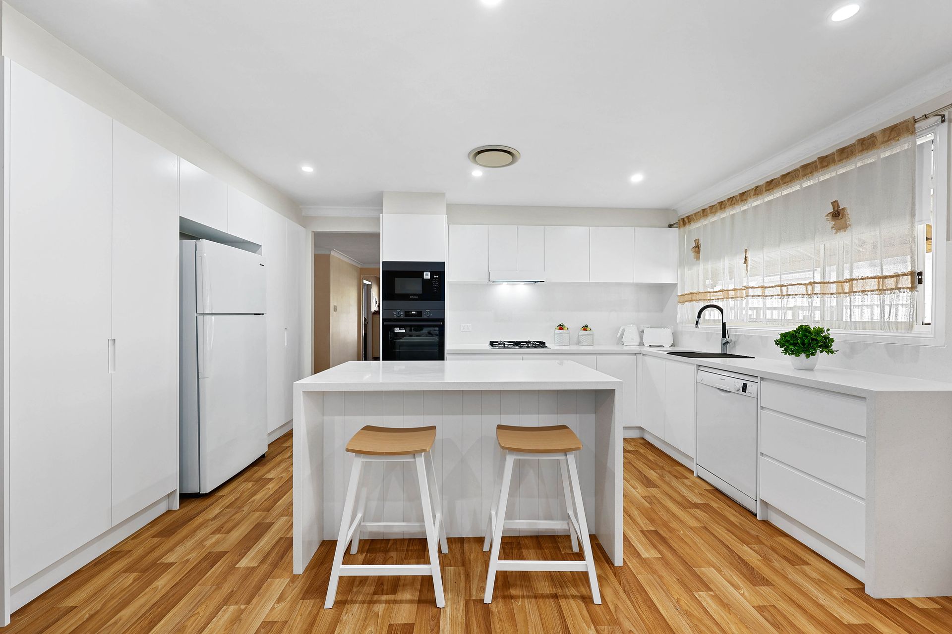 White kitchen with island, two stools, stainless steel appliances, and hardwood floors — Above & Beyond Interiors in Narellan, NSW