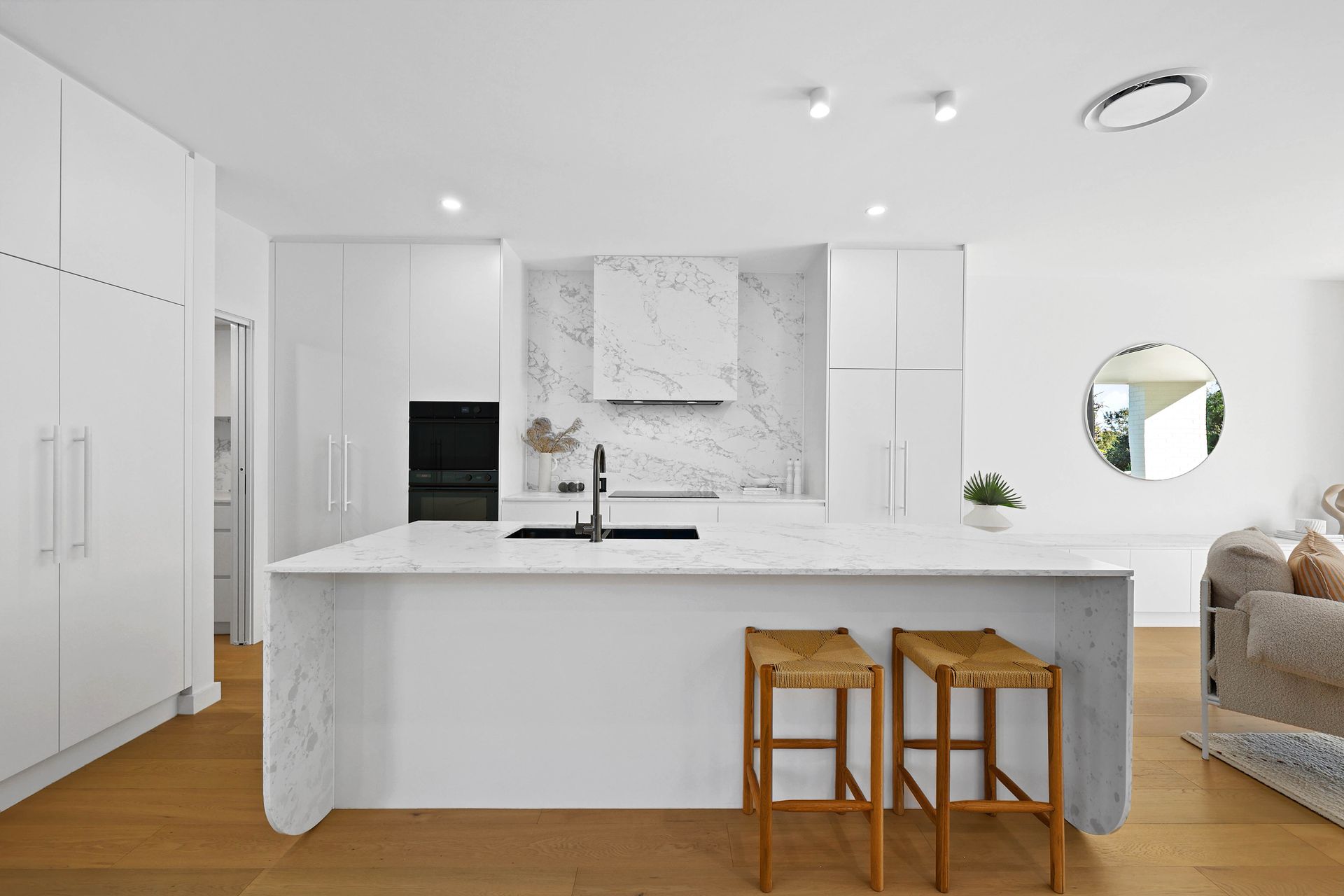 White modern kitchen with marble backsplash, island with stools, and wooden floor — Above & Beyond Interiors in Southern Highlands, NSW