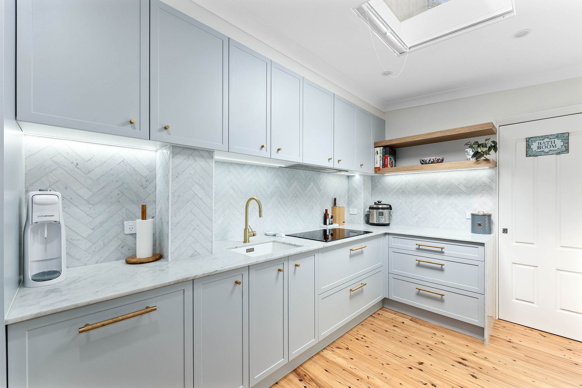 Light blue kitchen with gold accents and wooden floors — Above & Beyond Interiors in Mount Annan, NSW