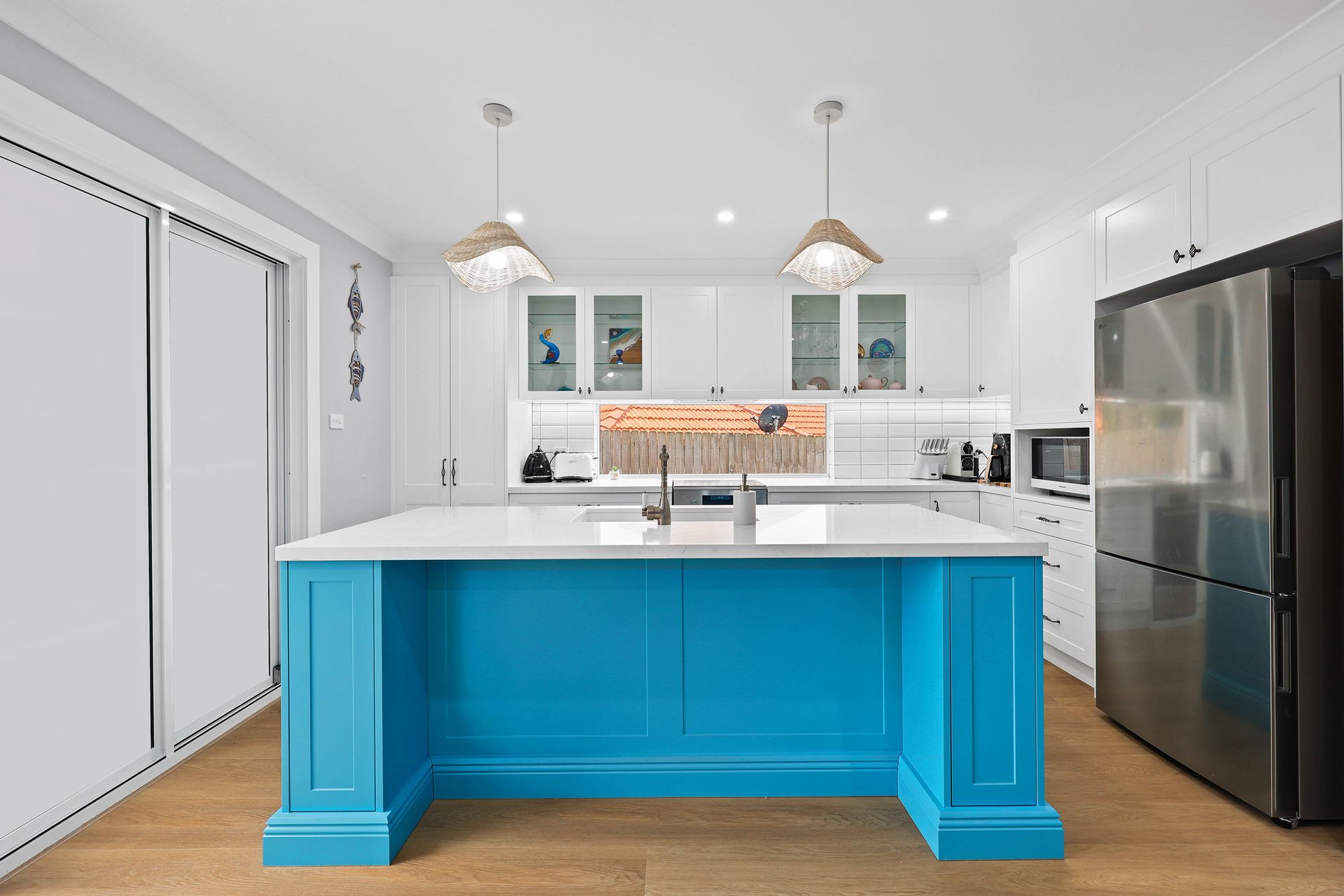 Bright kitchen with a blue island and white cabinets, wooden floor, stainless steel refrigerator — Above & Beyond Interiors in Southern Highlands, NSW