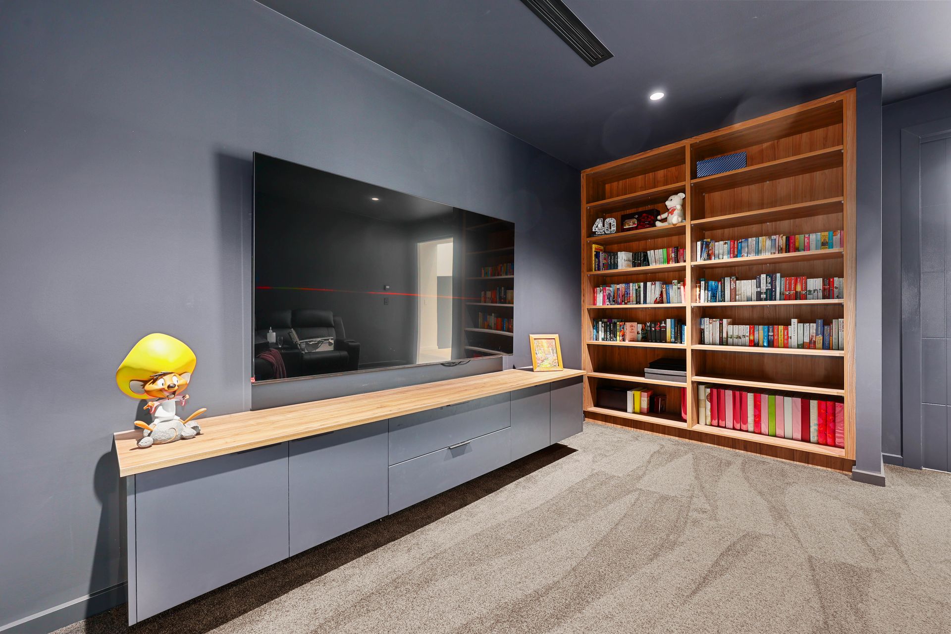 Grey entertainment unit with TV, wooden bookshelf, and figure in room with carpet — Above & Beyond Interiors in Smeaton Grange, NSW