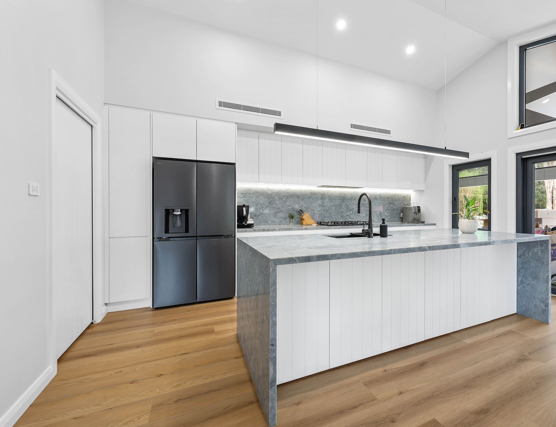 Modern white kitchen with island, stainless steel appliances, and hardwood floors — Above & Beyond Interiors Custom Joinery in Bellambi, NSW