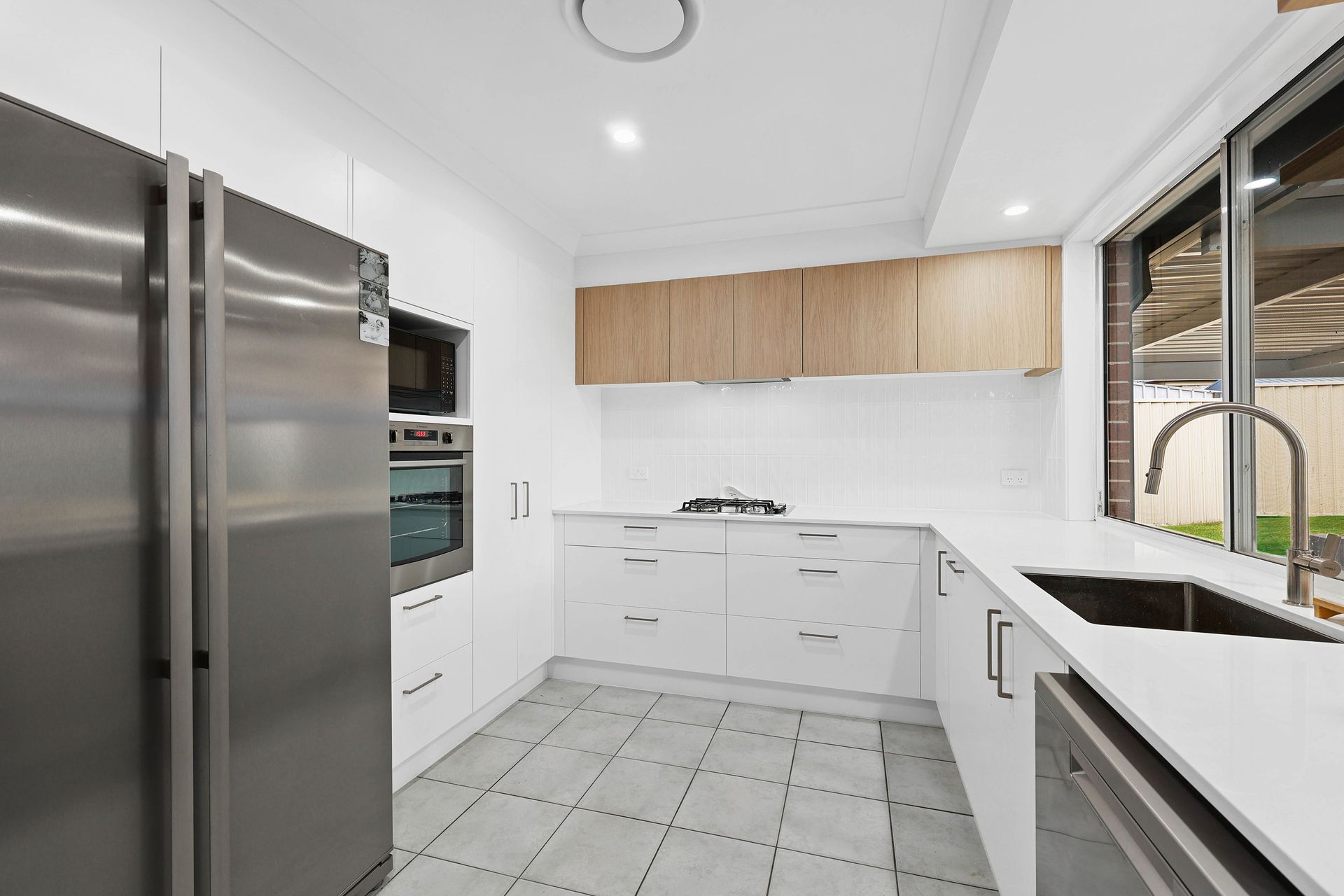 Modern kitchen with white cabinets, stainless steel appliances, and a window overlooking a yard — Above & Beyond Interiors in Narellan, NSW