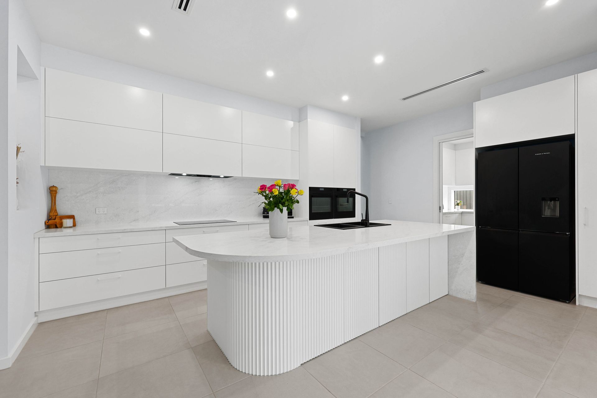 Modern white kitchen with curved island and black refrigerator — Above & Beyond Interiors in Narellan, NSW