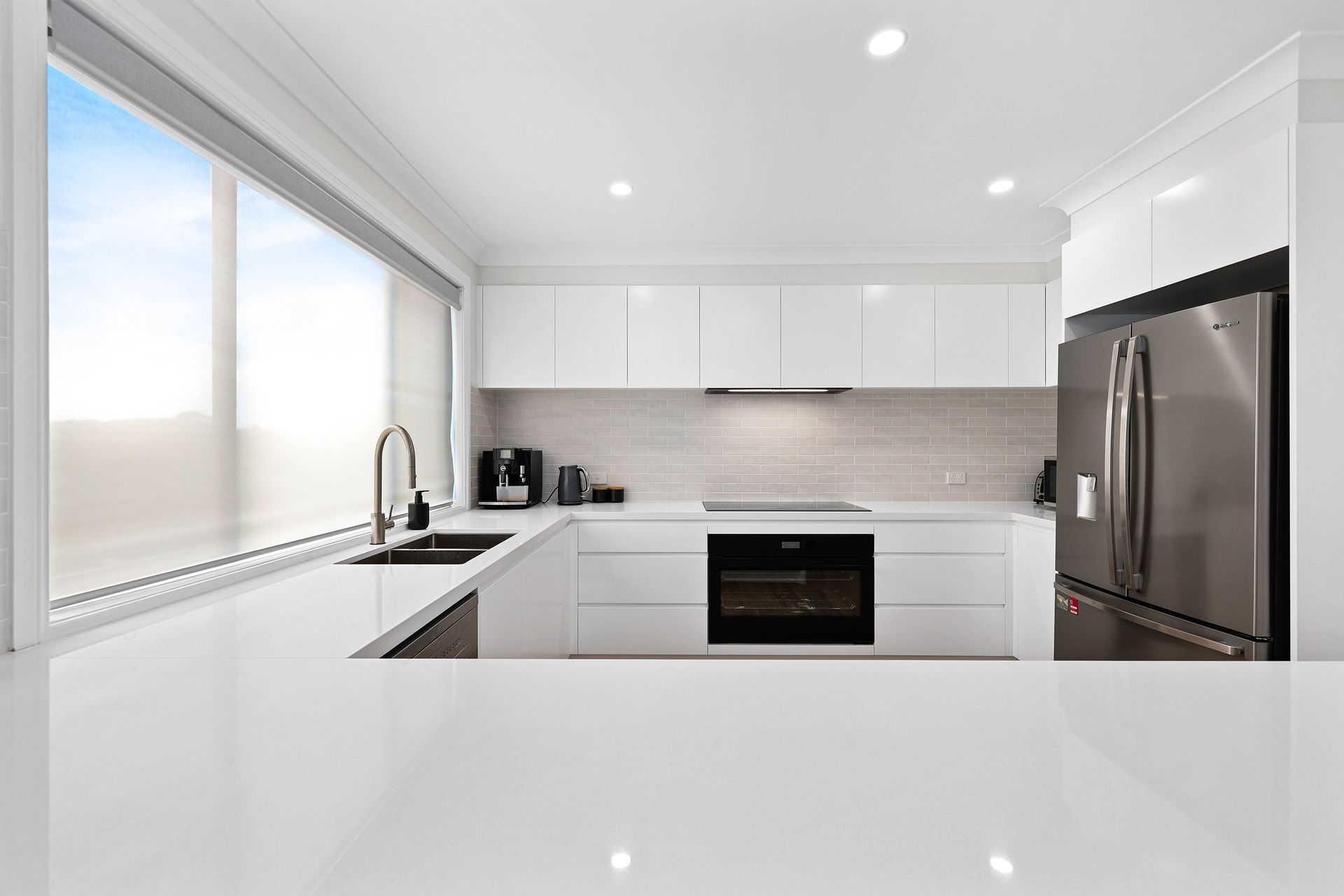 Modern, bright white kitchen with stainless steel appliances and large window — Above & Beyond Interiors in Mount Annan, NSW