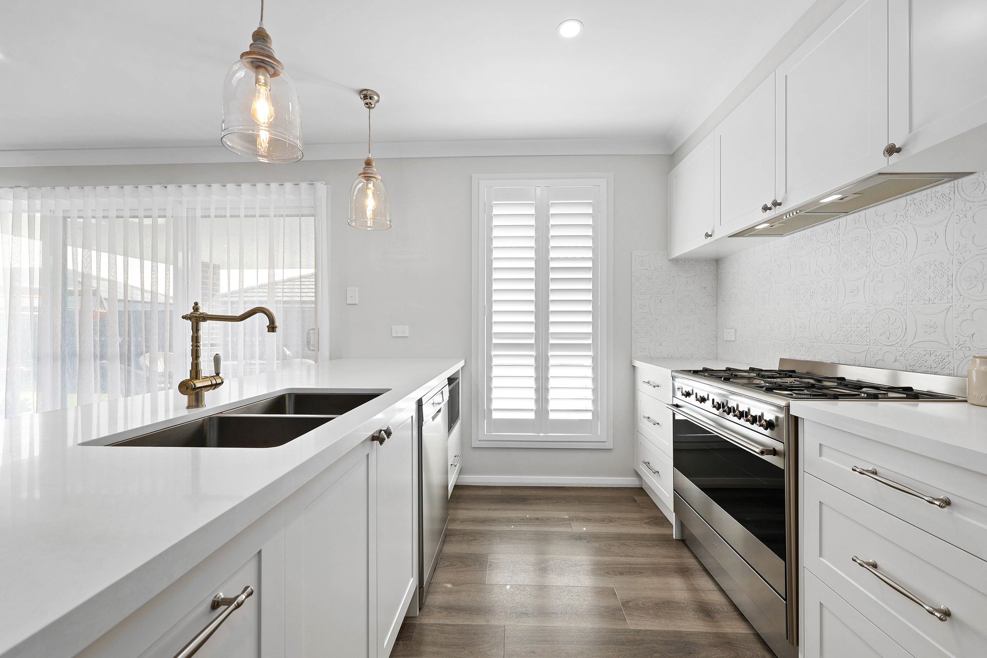 Modern white kitchen with island, sink, stainless steel appliances, and window shutters — Above & Beyond Interiors in Smeaton Grange, NSW