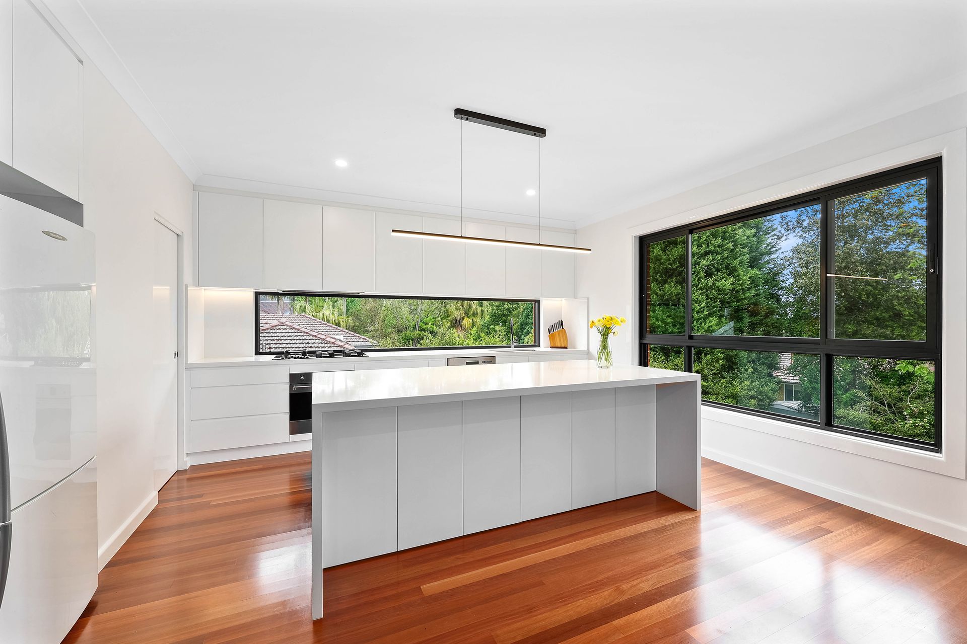 Modern white kitchen with wooden floors and large windows overlooking greenery — Above & Beyond Interiors in Smeaton Grange, NSW
