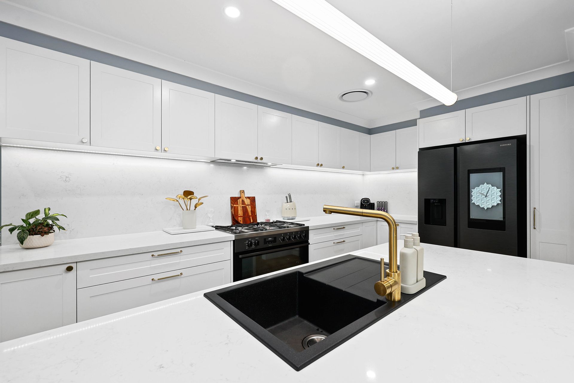 Modern white kitchen with black sink, gold faucet, and black refrigerator — Above & Beyond Interiors in Narellan, NSW