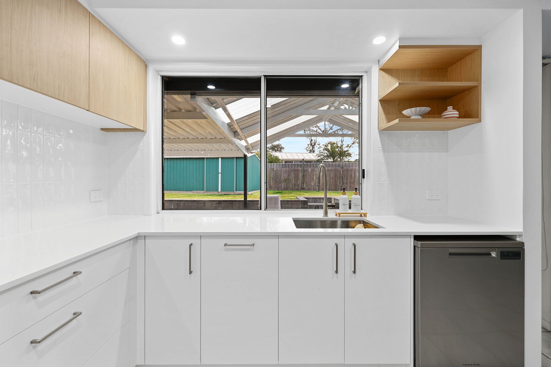 Modern kitchen with white cabinets, stainless steel sink, dishwasher, and a view of a backyard  — Above & Beyond Interiors in Smeaton Grange, NSW