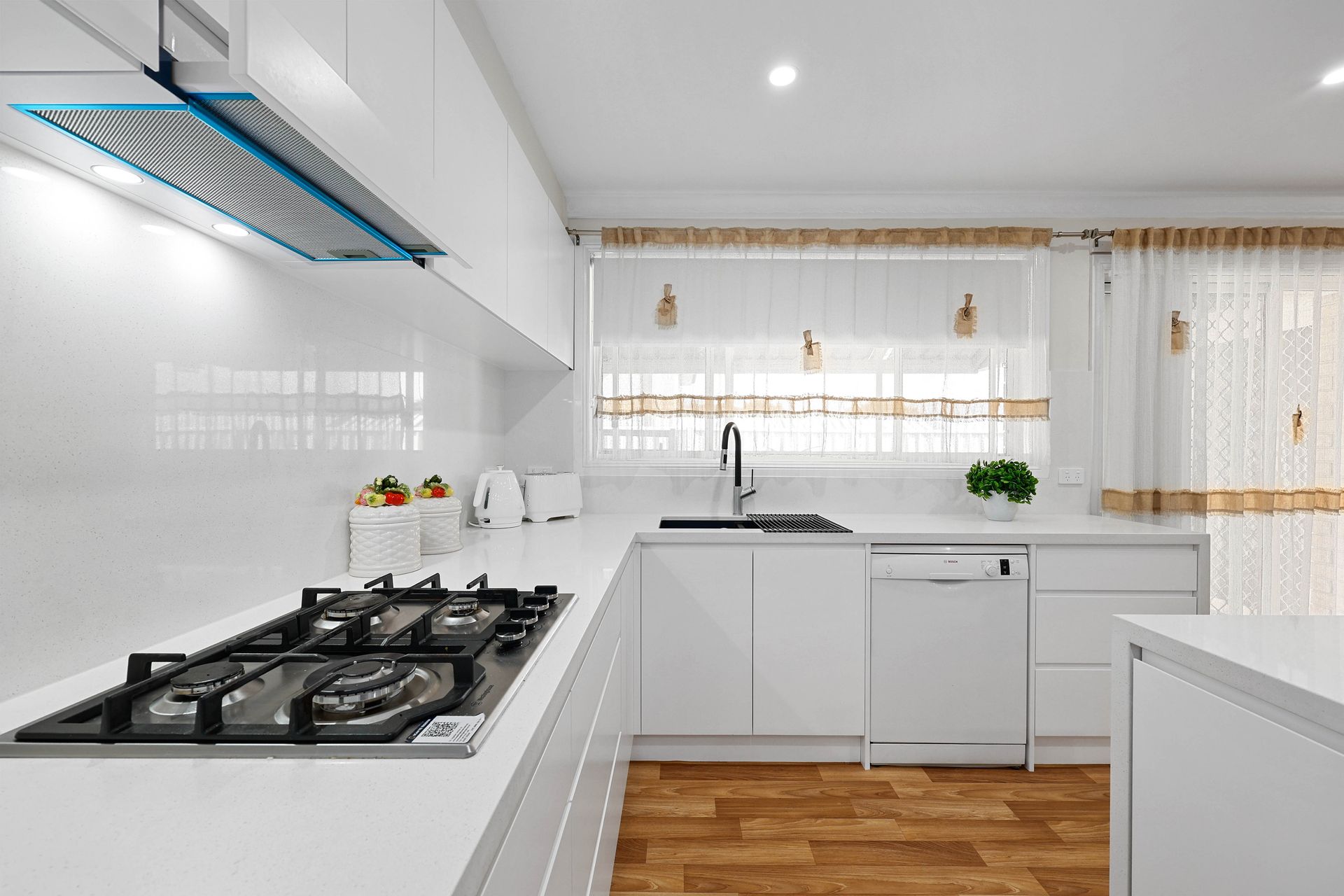 White modern kitchen with gas stovetop, sink, and window with sheer curtains — Above & Beyond Interiors in Narellan, NSW