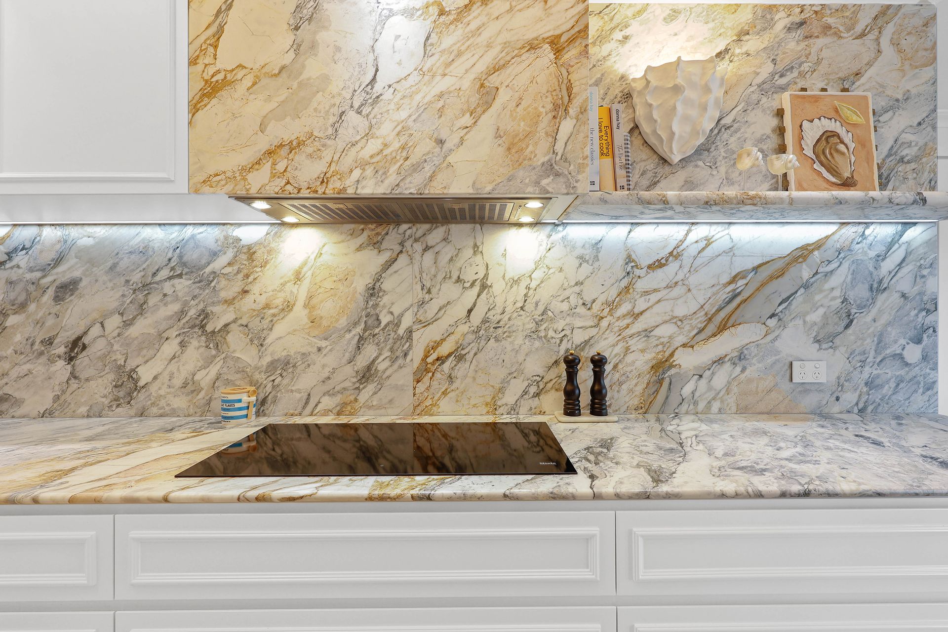 Kitchen with white cabinets, granite countertops and backsplash, and modern cooktop — Above & Beyond Interiors in Southern Highlands, NSW