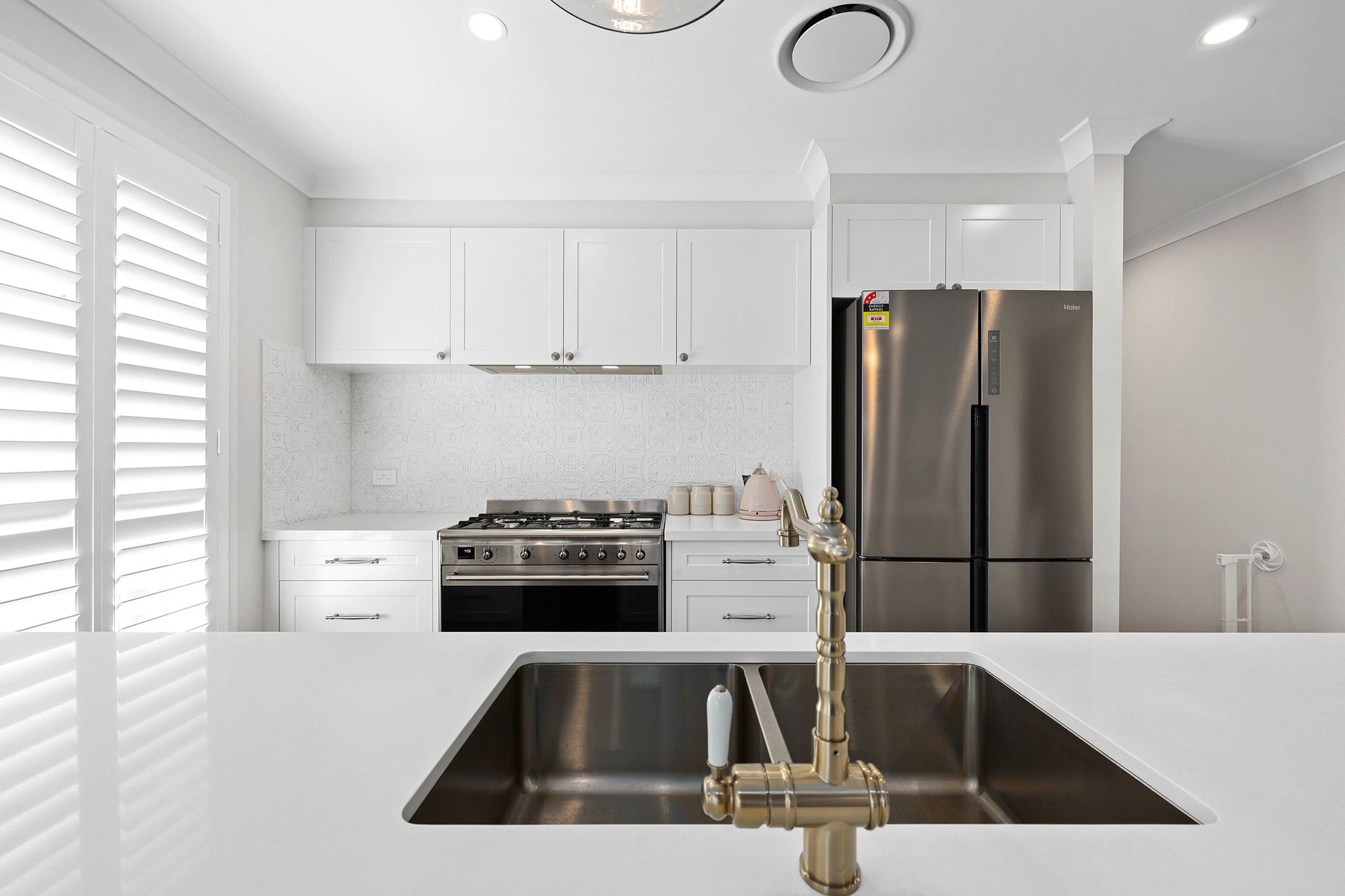 White kitchen with stainless steel appliances, gold faucet, and white countertops — Above & Beyond Interiors in Picton, NSW