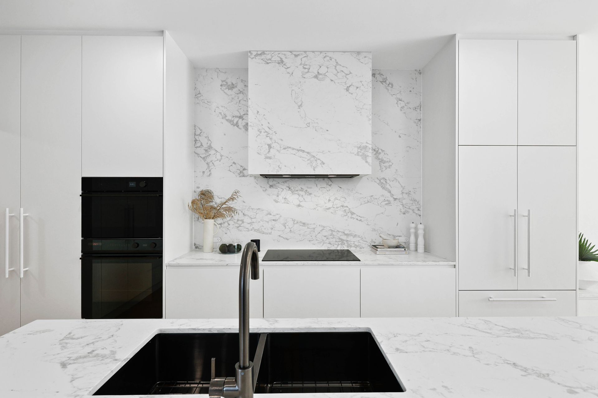 Modern white kitchen with marble backsplash, black sink and appliances — Above & Beyond Interiors in Southern Highlands, NSW