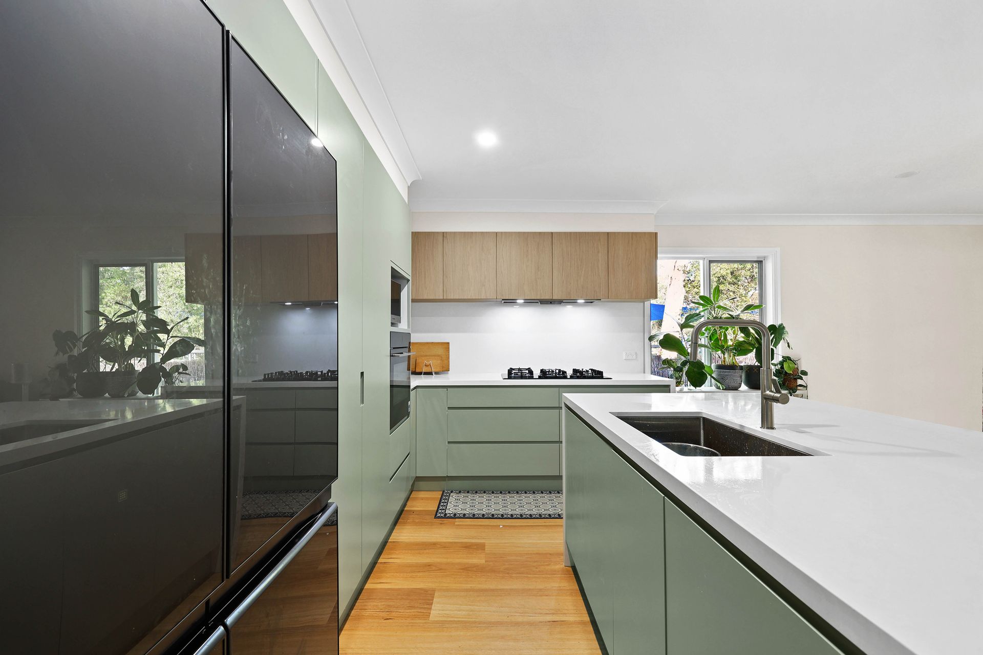 Modern kitchen with sage green cabinets, wooden upper cabinets, and a white island with a sink — Above & Beyond Interiors in Picton, NSW