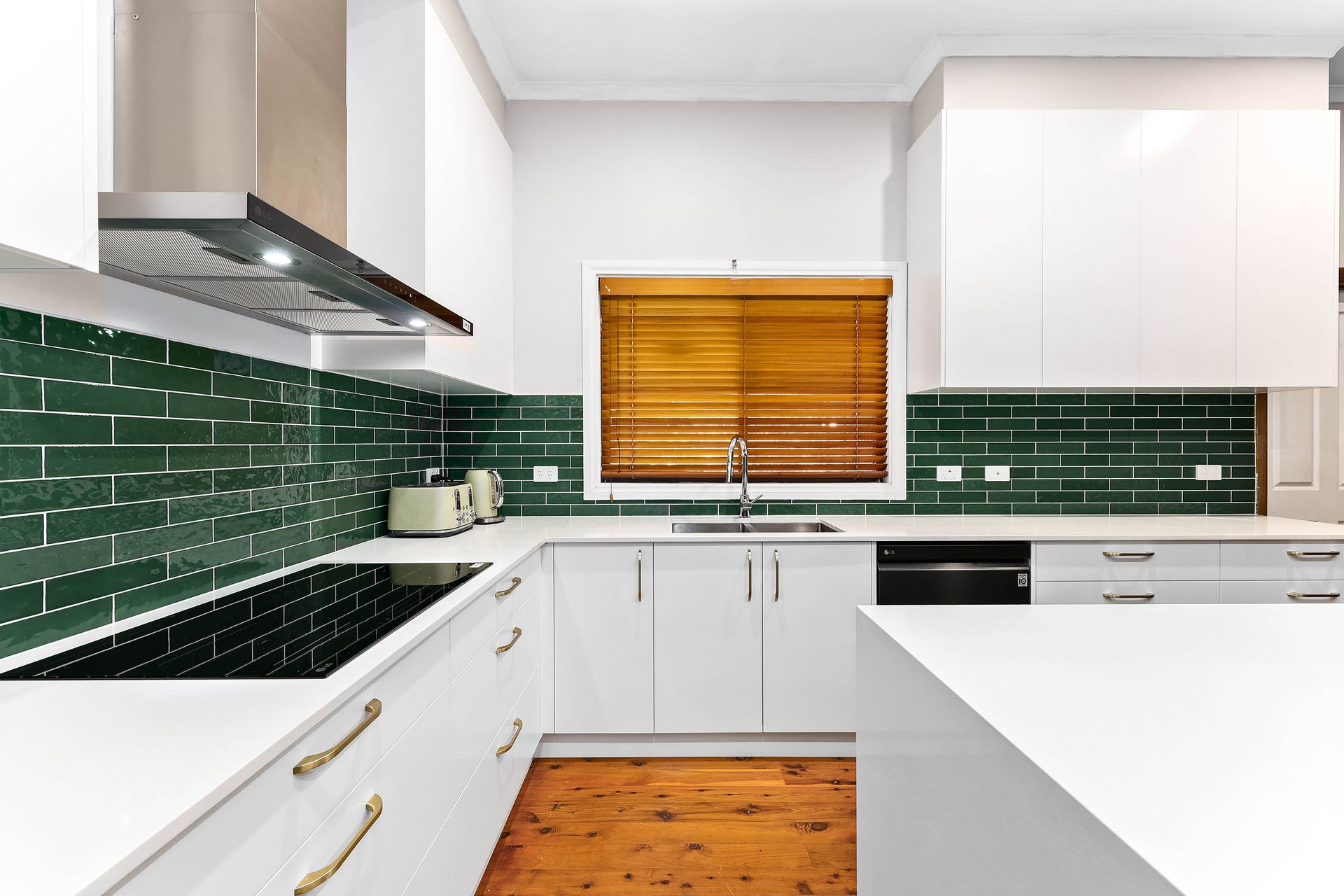 Modern white kitchen with green tiled backsplash, wooden blinds, and gold hardware — Above & Beyond Interiors in Picton, NSW