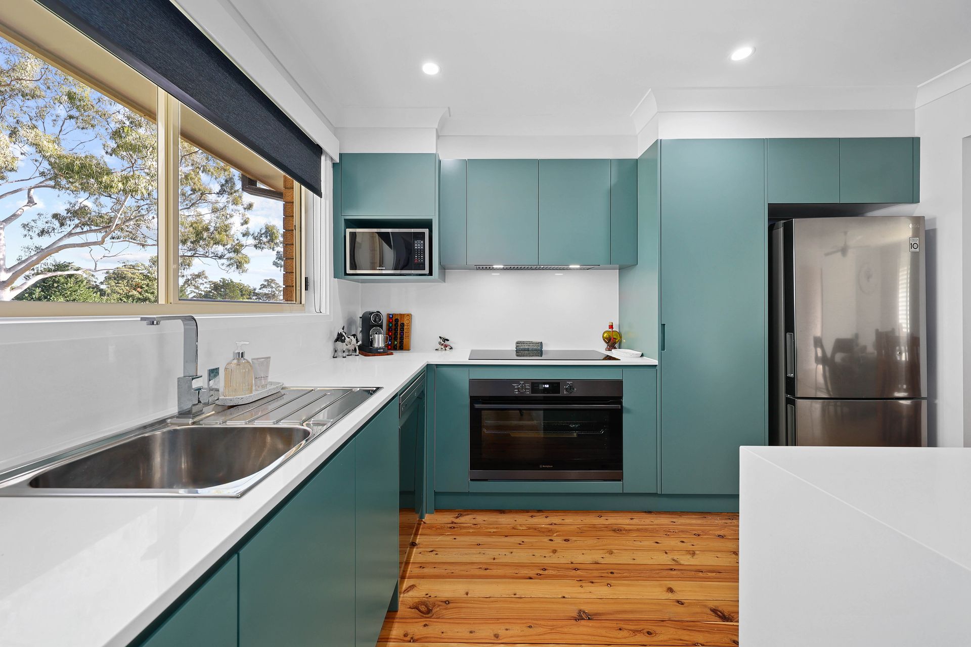 Teal kitchen with stainless steel appliances, white countertops, and wood flooring next to a window — Above & Beyond Interiors in Southern Highlands, NSW