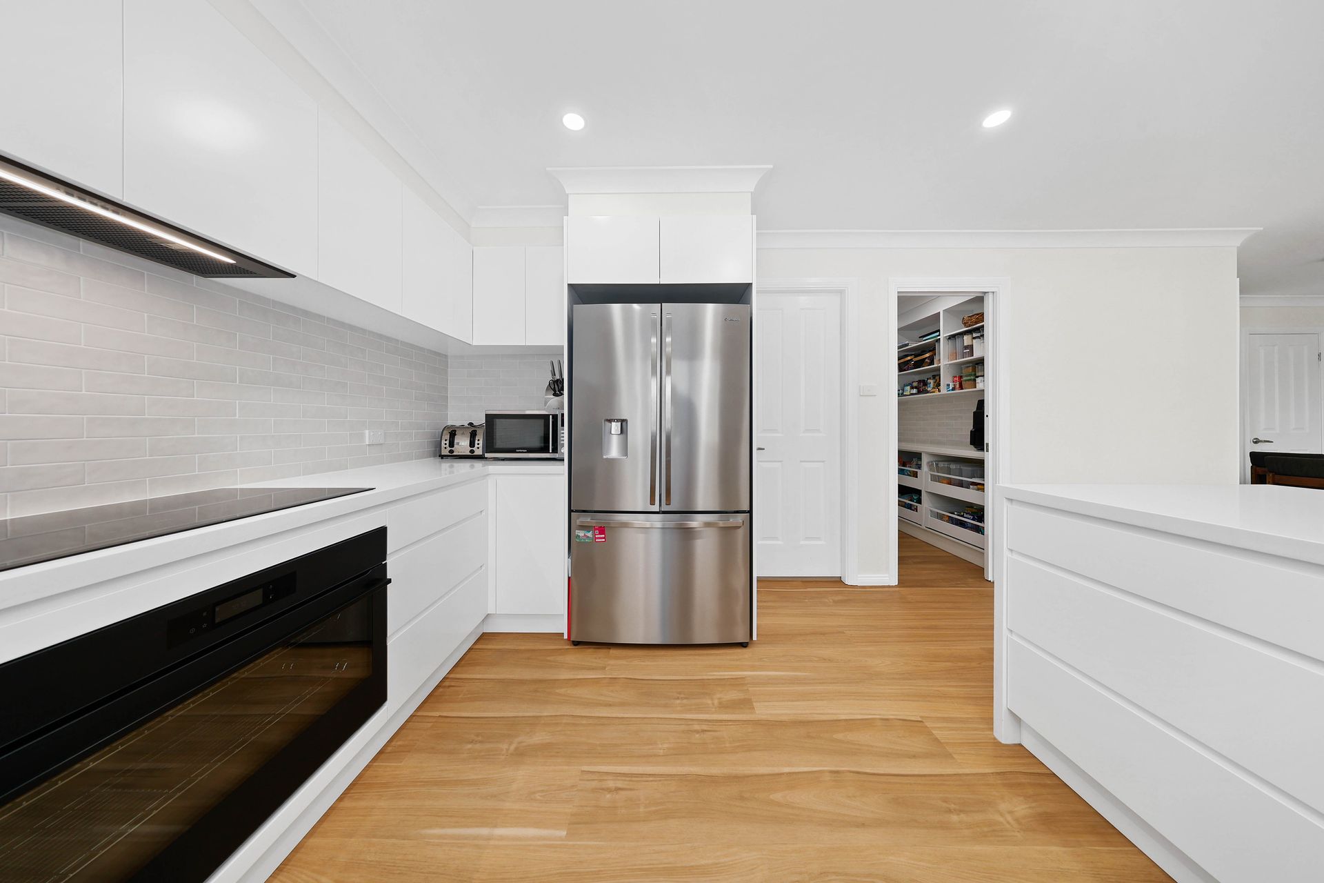 White modern kitchen with stainless steel appliances, wood floors, and pantry — Above & Beyond Interiors in Mount Annan, NSW