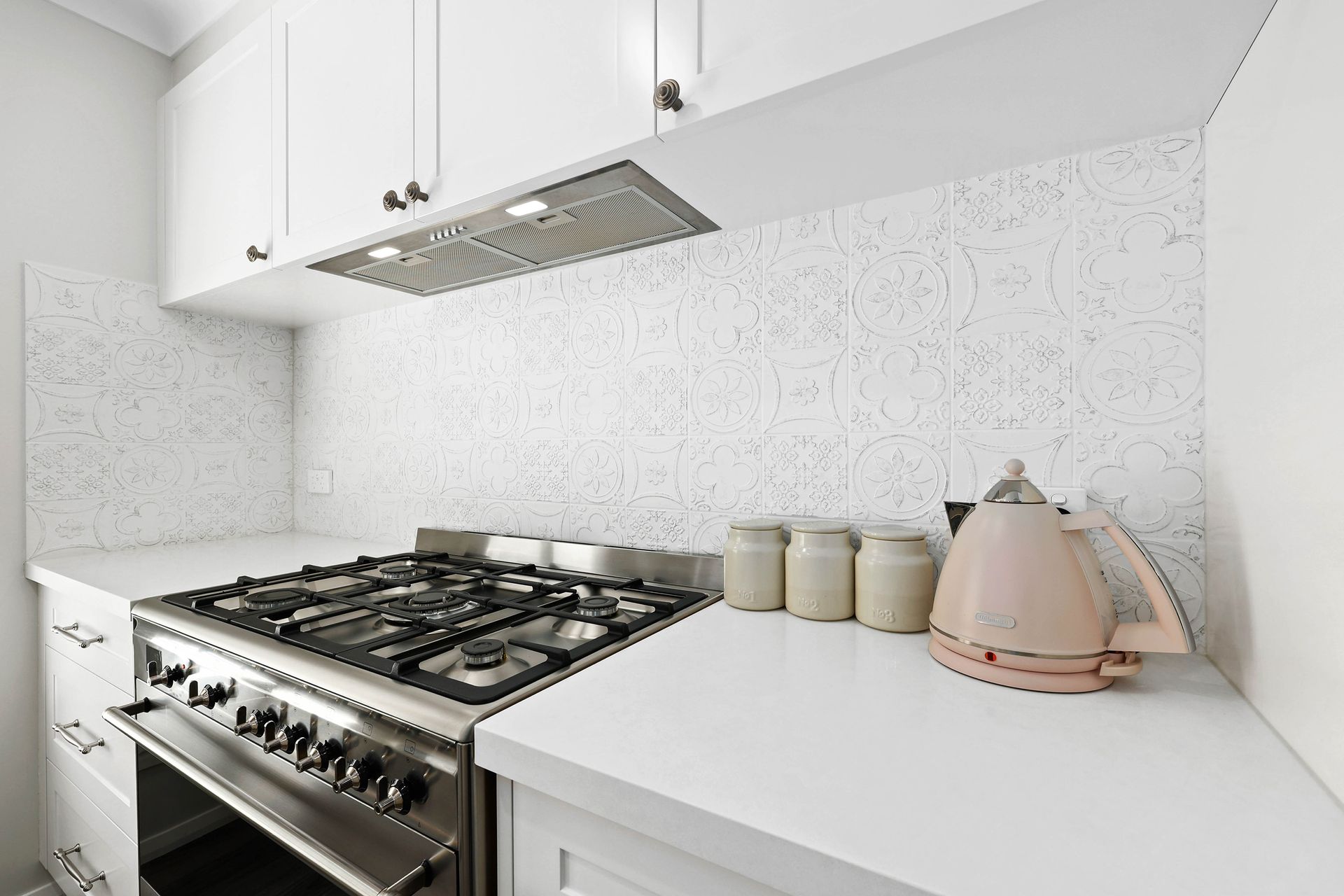 White kitchen with a stove, range hood, and a pink kettle on the counter — Above & Beyond Interiors in Smeaton Grange, NSW