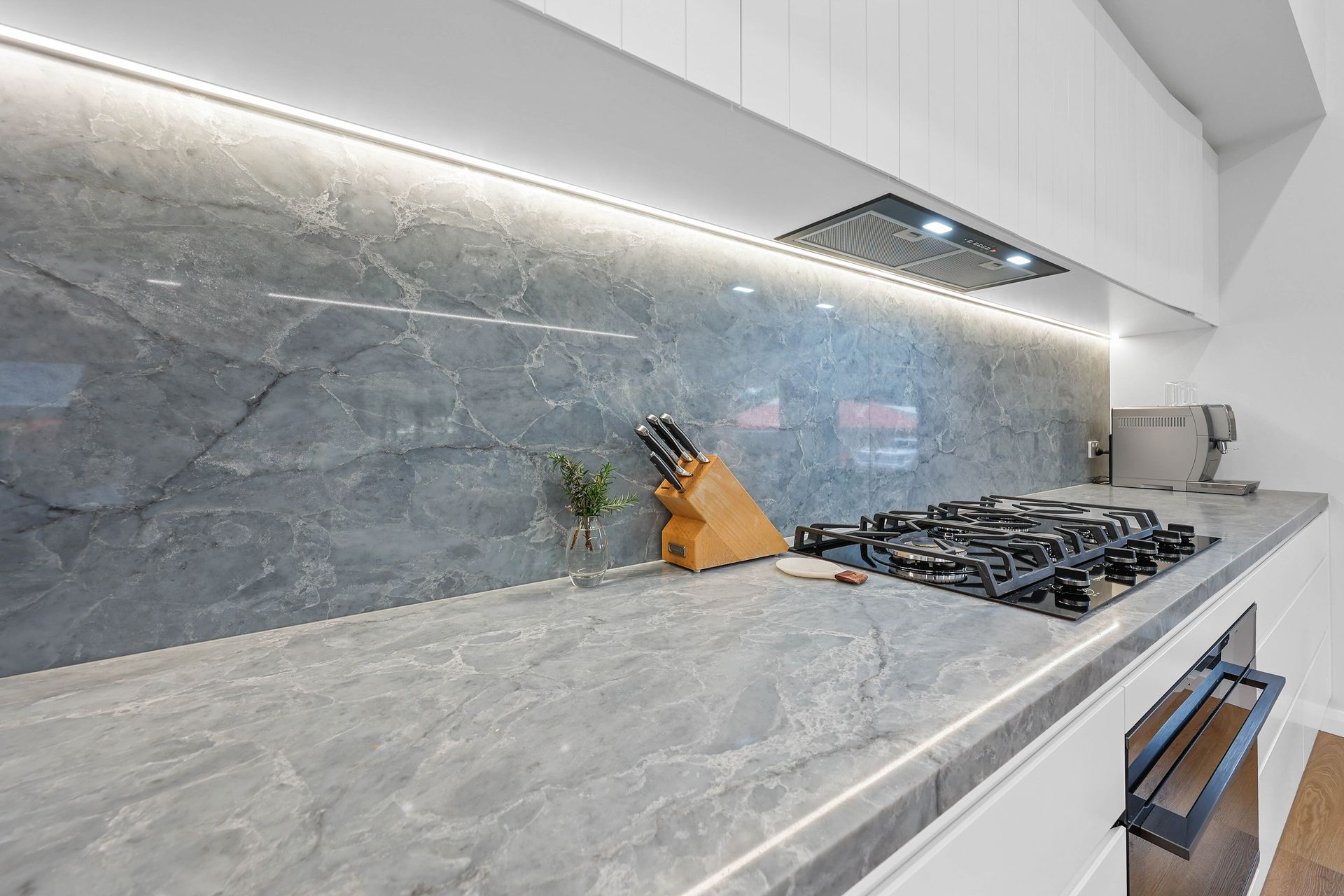 Modern kitchen with grey marble countertop and backsplash, built-in gas cooktop, and under-cabinet lighting — Above & Beyond Interiors in Wollongong, NSW