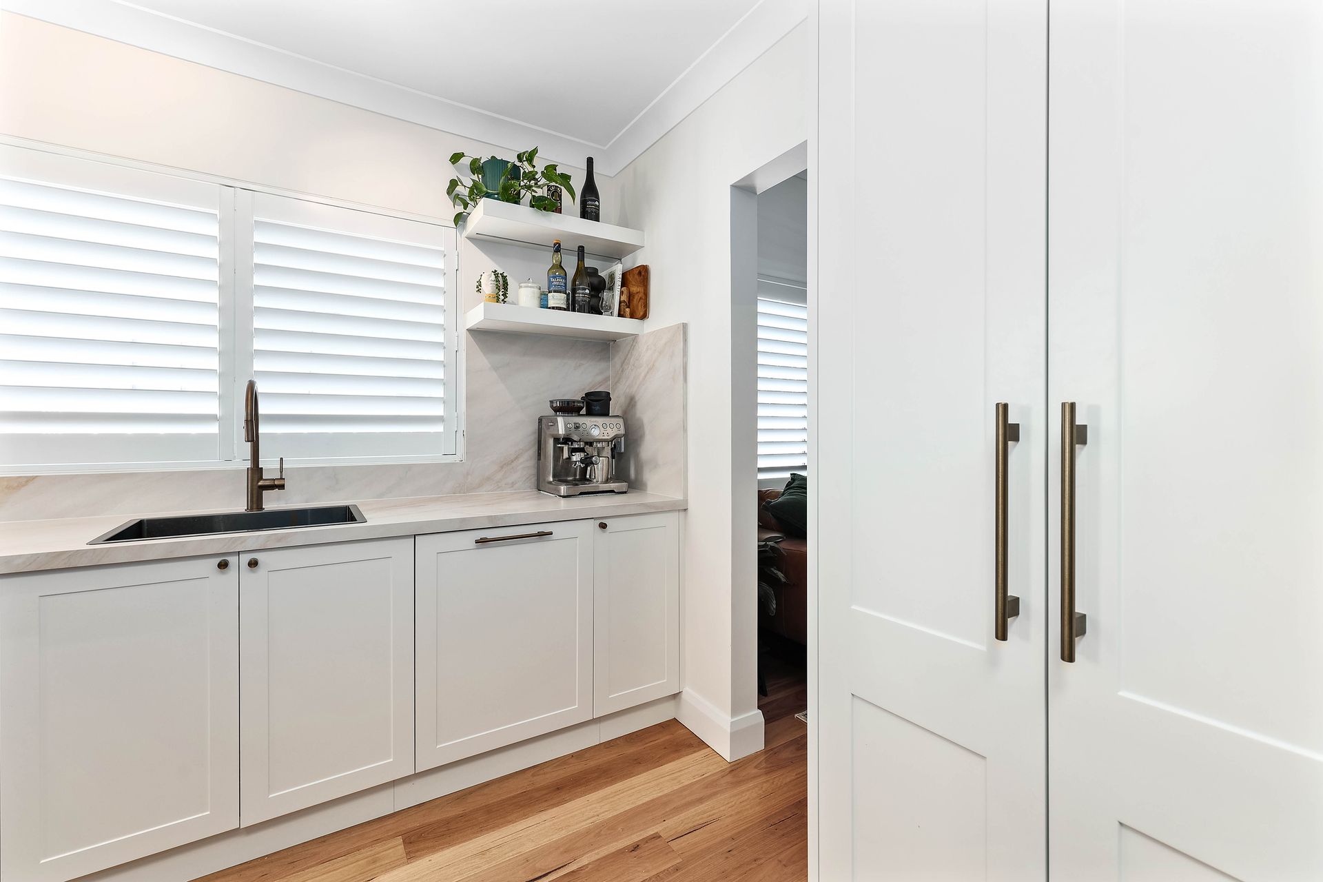 White kitchen with cabinets, sink, open shelving, and a doorway; light wood floor  — Above & Beyond Interiors in Smeaton Grange, NSW