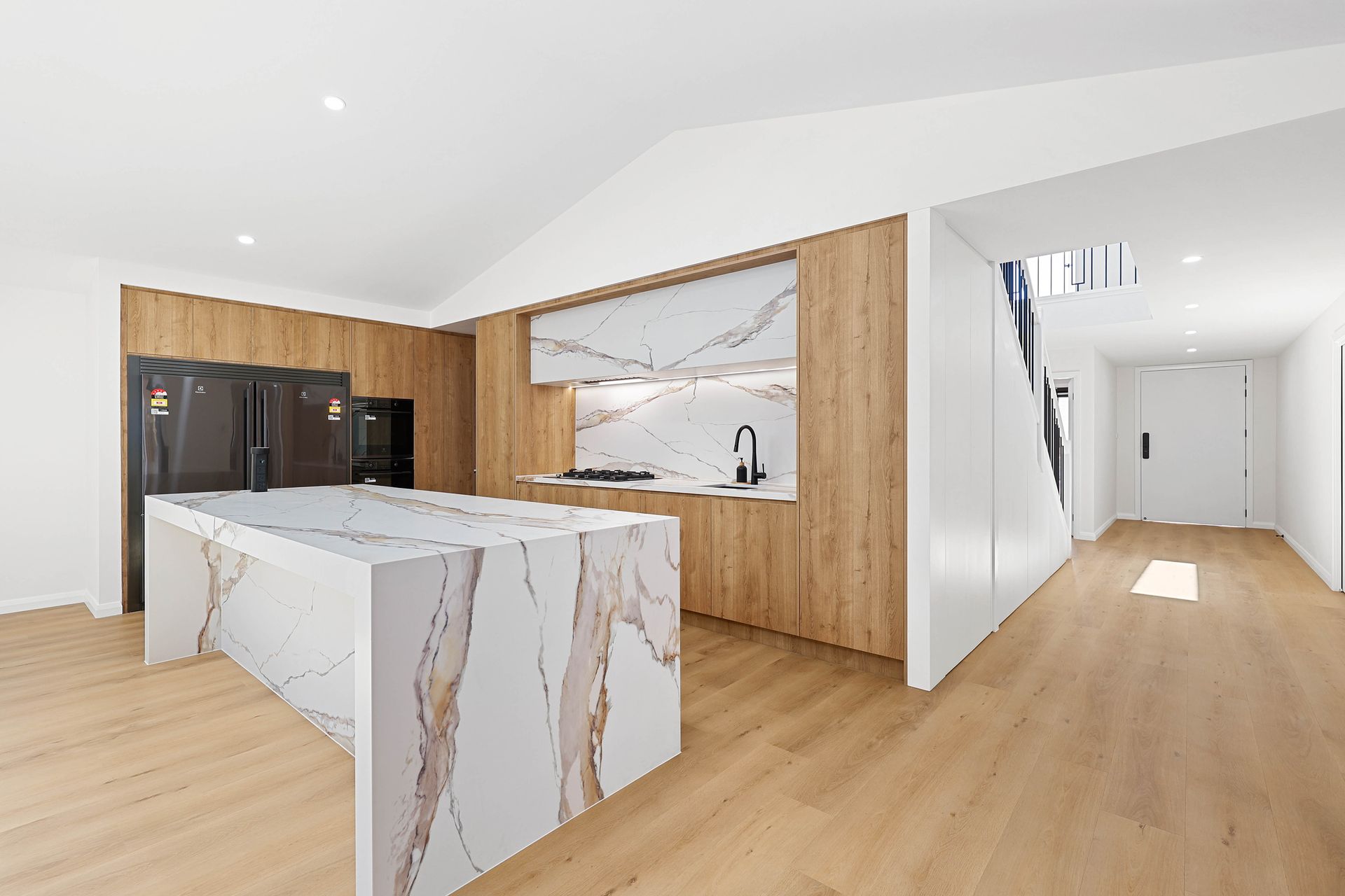 Modern kitchen with a marble island and light wood cabinets. Includes two black refrigerators — Above & Beyond Interiors in Southern Highlands, NSW