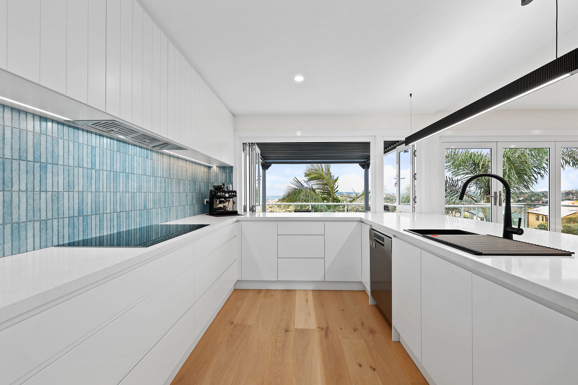 Modern white kitchen with wood floors, blue tiled backsplash, and large windows — Above & Beyond Interiors in Southern Highlands, NSW