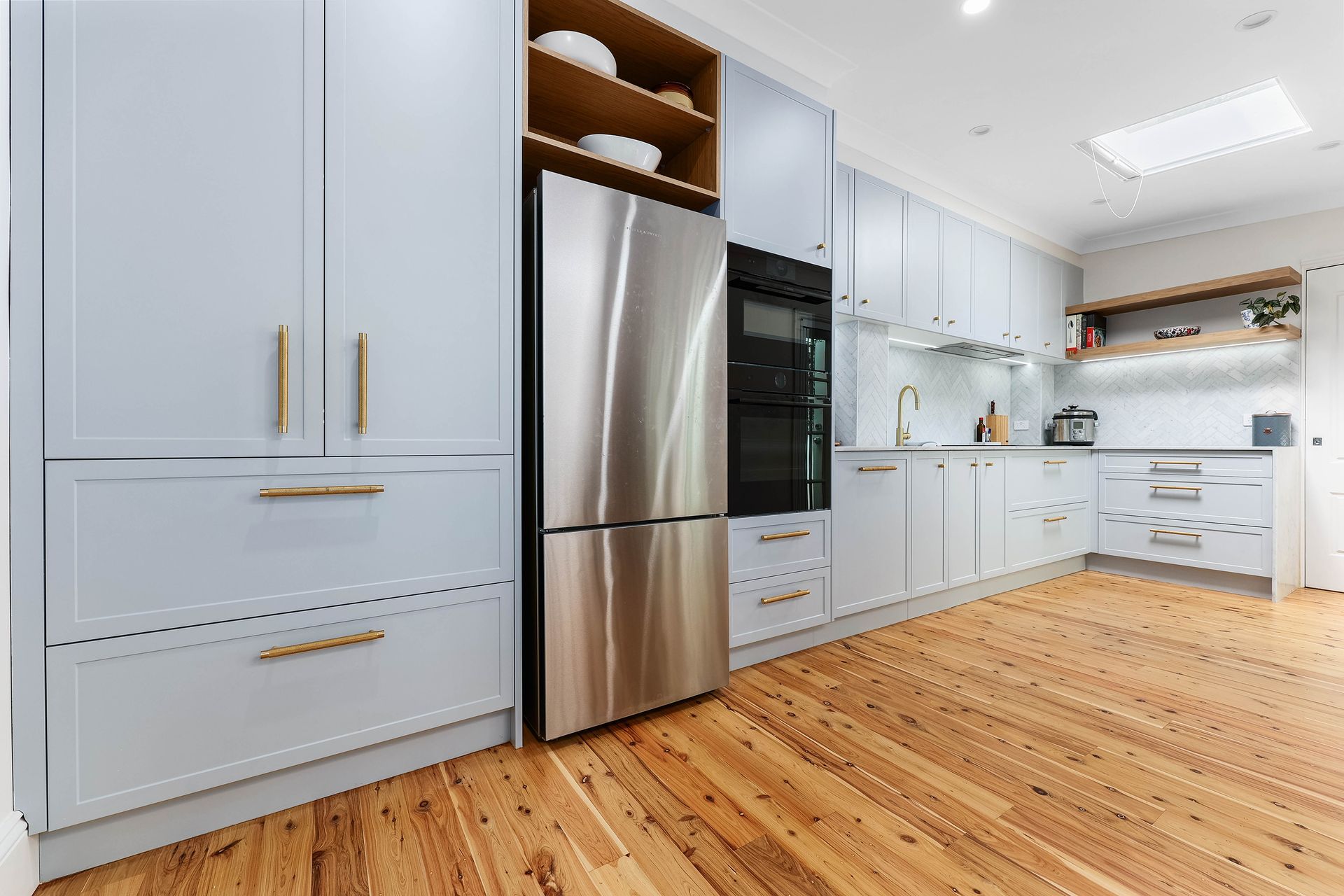 Light blue kitchen with stainless steel appliances, wooden floor, and light-filled skylight — Above & Beyond Interiors in Smeaton Grange, NSW