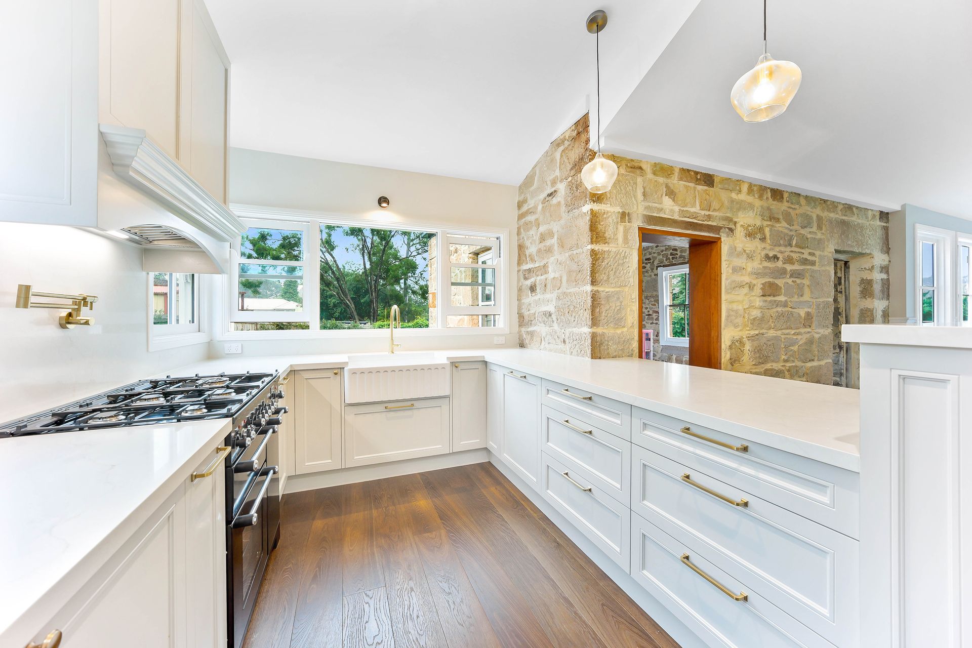 Bright, modern kitchen with white cabinets, stone wall, and wooden floor — Above & Beyond Interiors in Wollongong, NSW