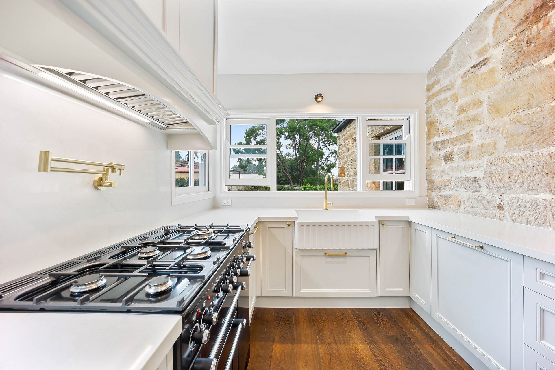 Kitchen with a stone wall, white cabinets, and a large black stovetop — Above & Beyond Interiors in Smeaton Grange, NSW