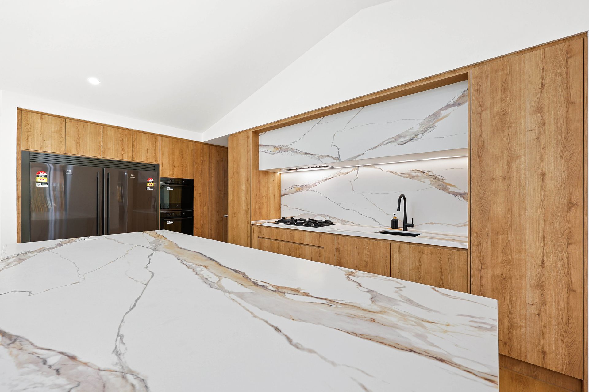 A Kitchen with White Marble Island and Wood Cabinetry — Above & Beyond Interiors in Smeaton Grange, NSW