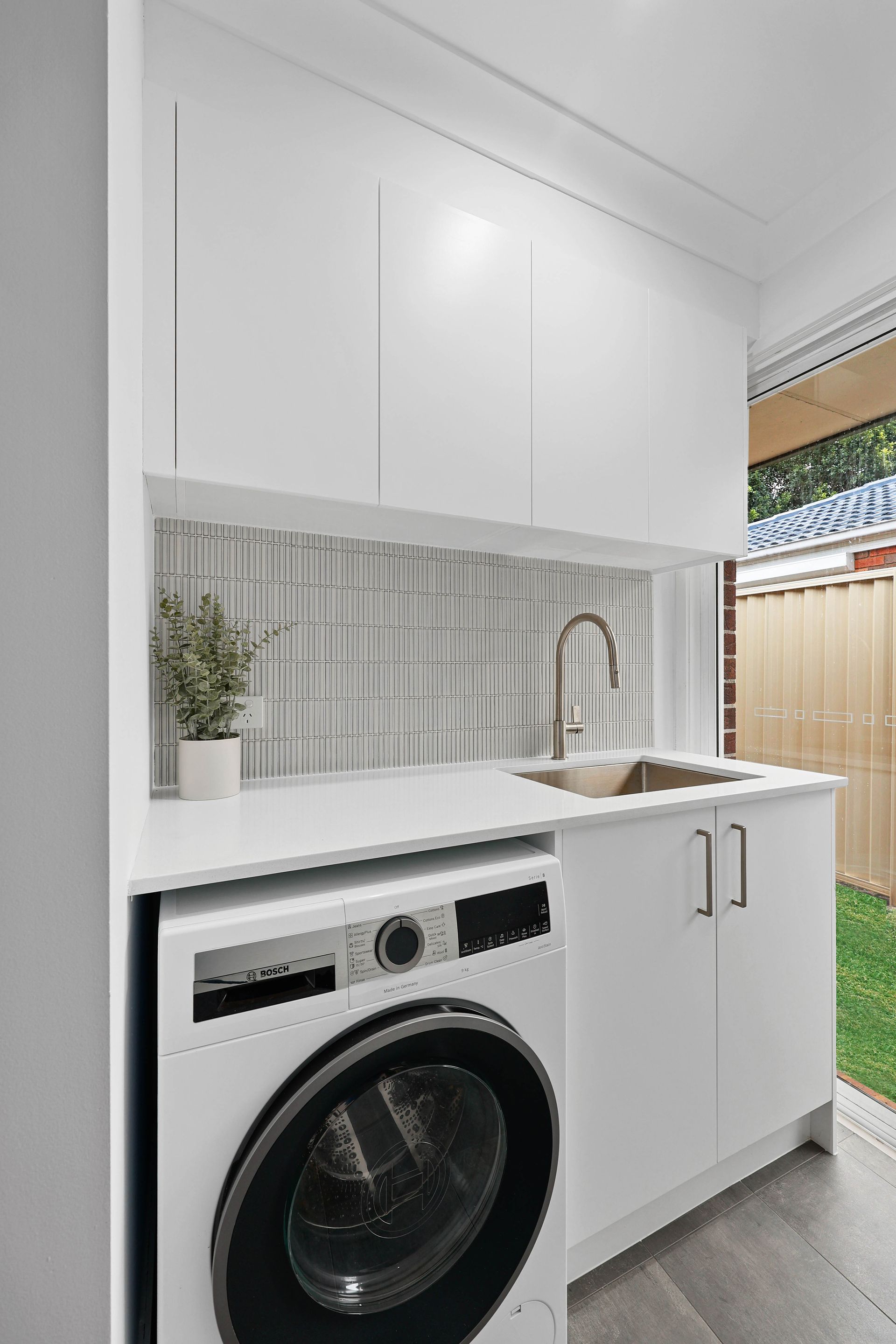 Modern white laundry room with washing machine, sink, and cabinets — Above & Beyond Interiors in Smeaton Grange, NSW