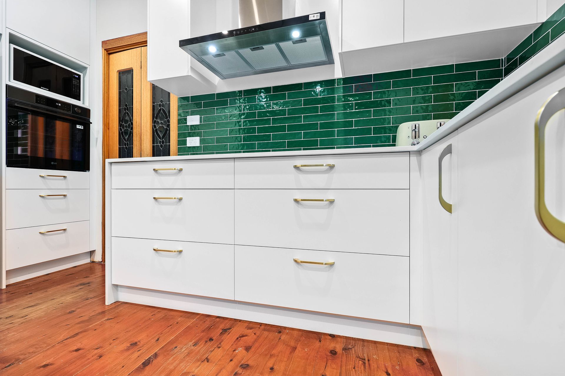 Modern White Kitchen with Green Tile Backsplash, Built-In Oven, and Wooden Floor — Above & Beyond Interiors in Smeaton Grange, NSW
