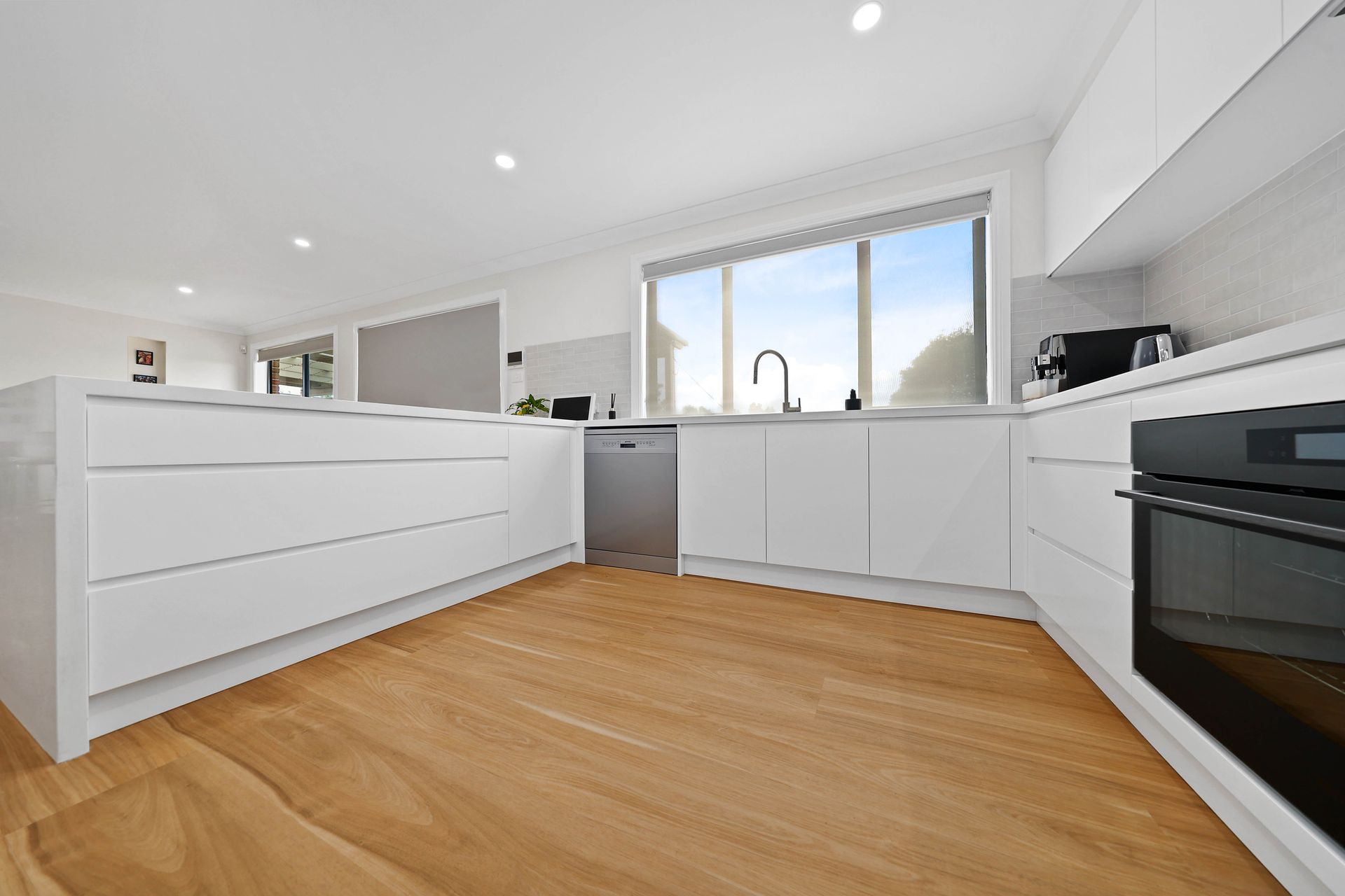 A White Kitchen with Wood Floor — Above & Beyond Interiors in Smeaton Grange, NSW